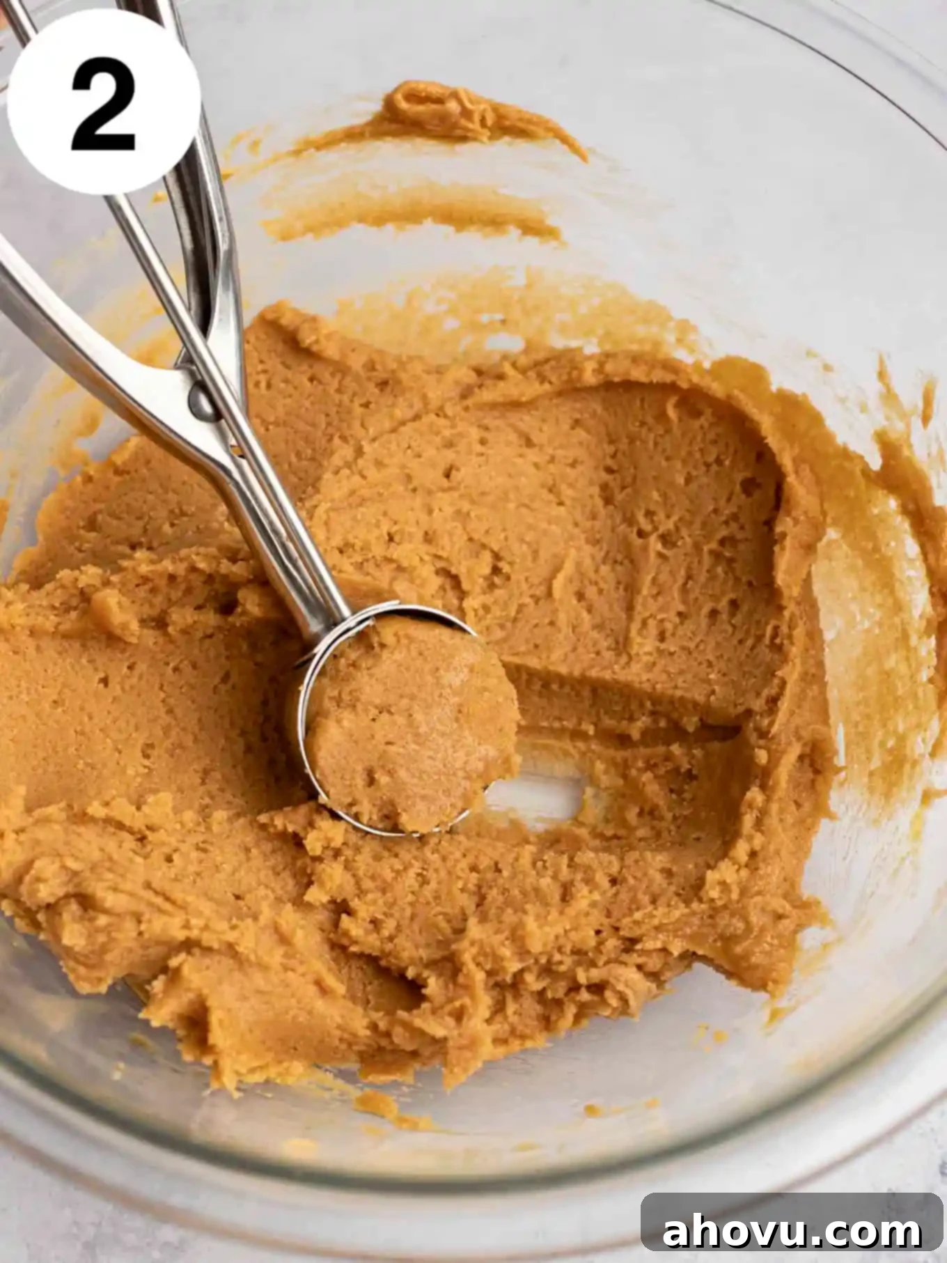Peanut butter cookie dough being scooped out of a glass mixing bowl.
