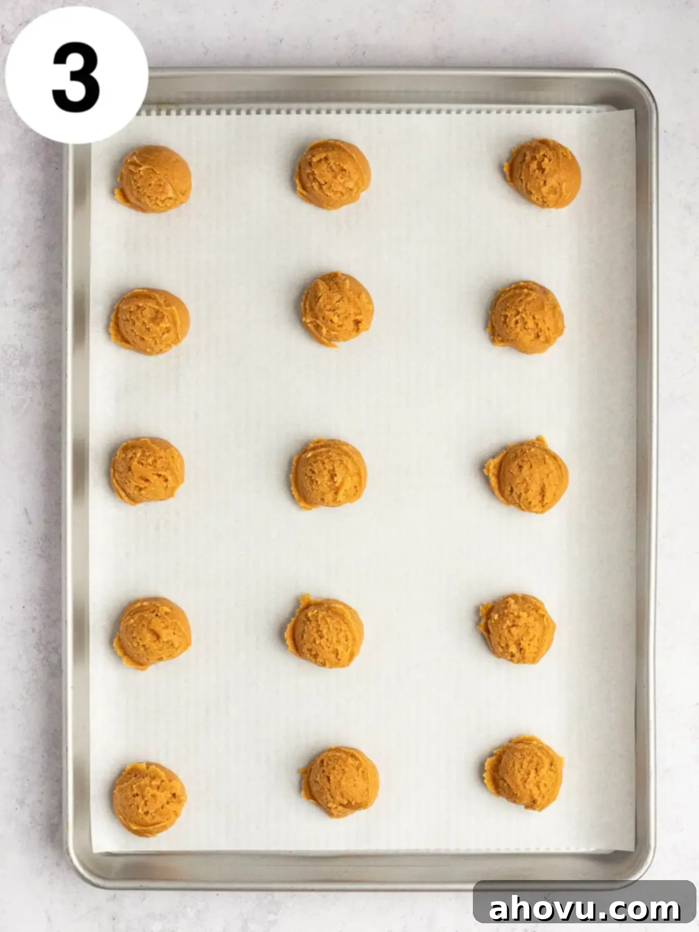 An overhead view of peanut butter cookie dough balls on a parchment lined baking sheet. 