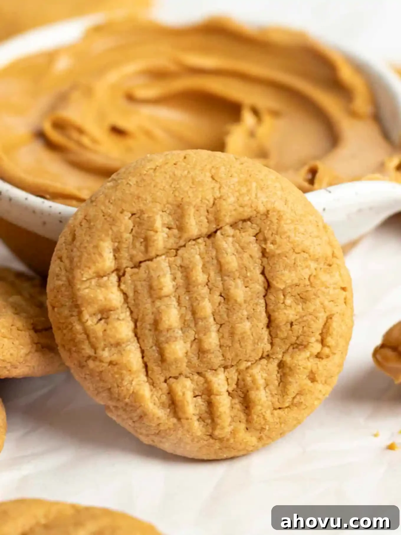A peanut butter cookie leaning against a dish of peanut butter. 