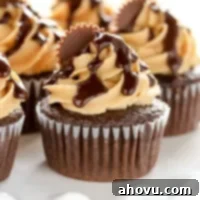 A top-down view of a beautifully frosted chocolate peanut butter cupcake with chocolate ganache and a miniature peanut butter cup, resting on a white surface.