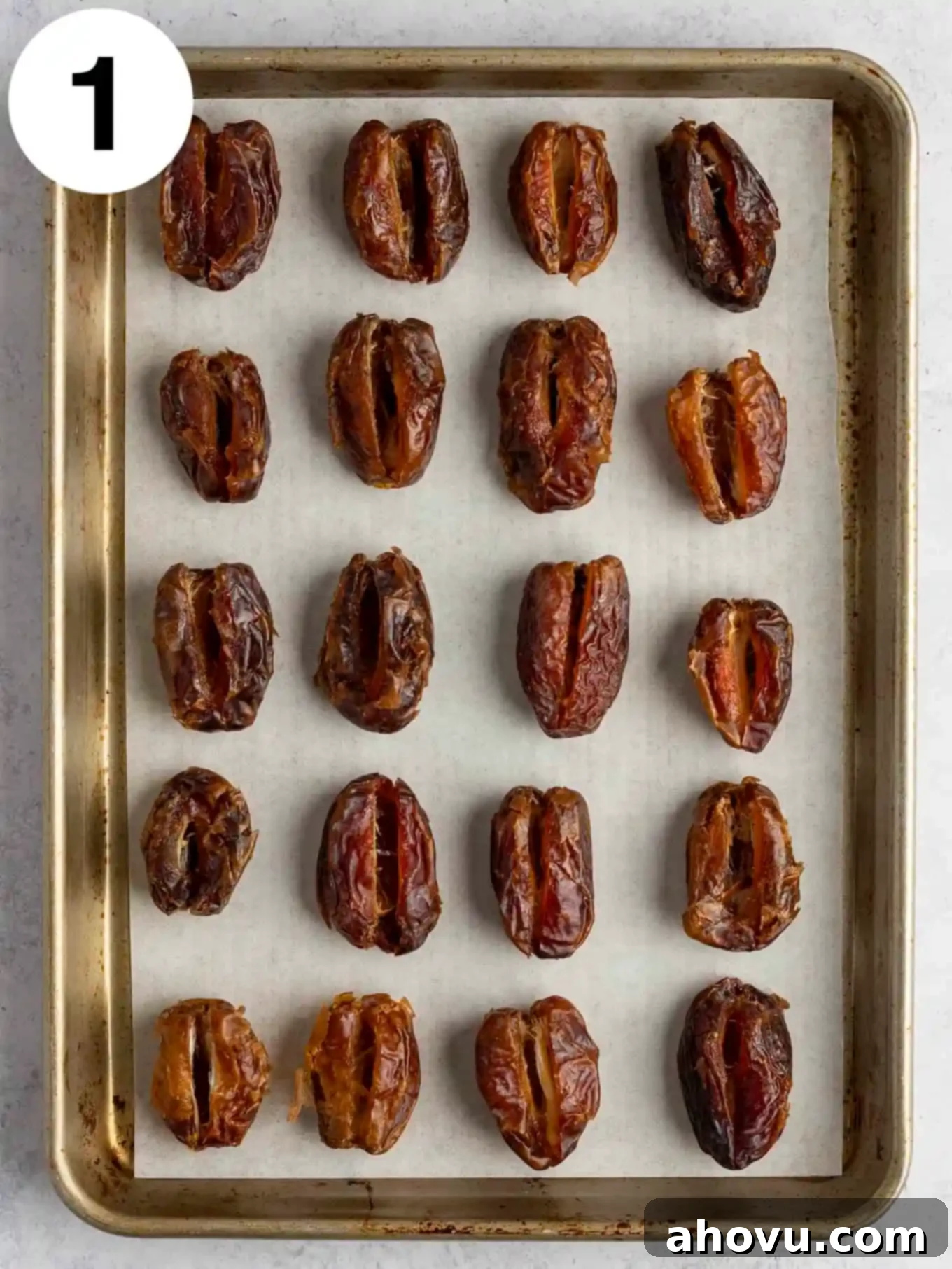 An overhead view of pitted dates lined up on a baking sheet. 