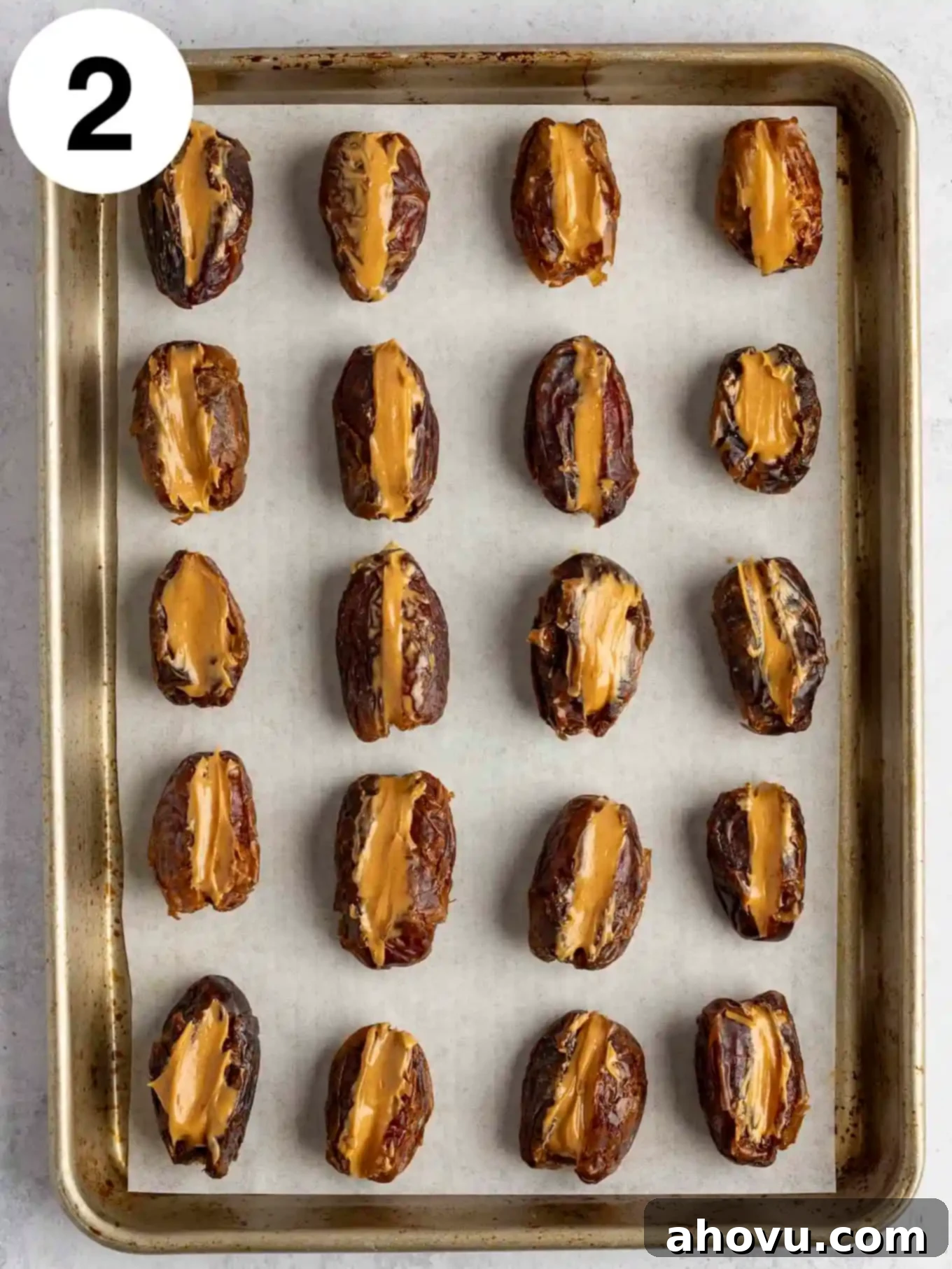 An overhead view of peanut butter stuffed dates lined up on a baking sheet. 