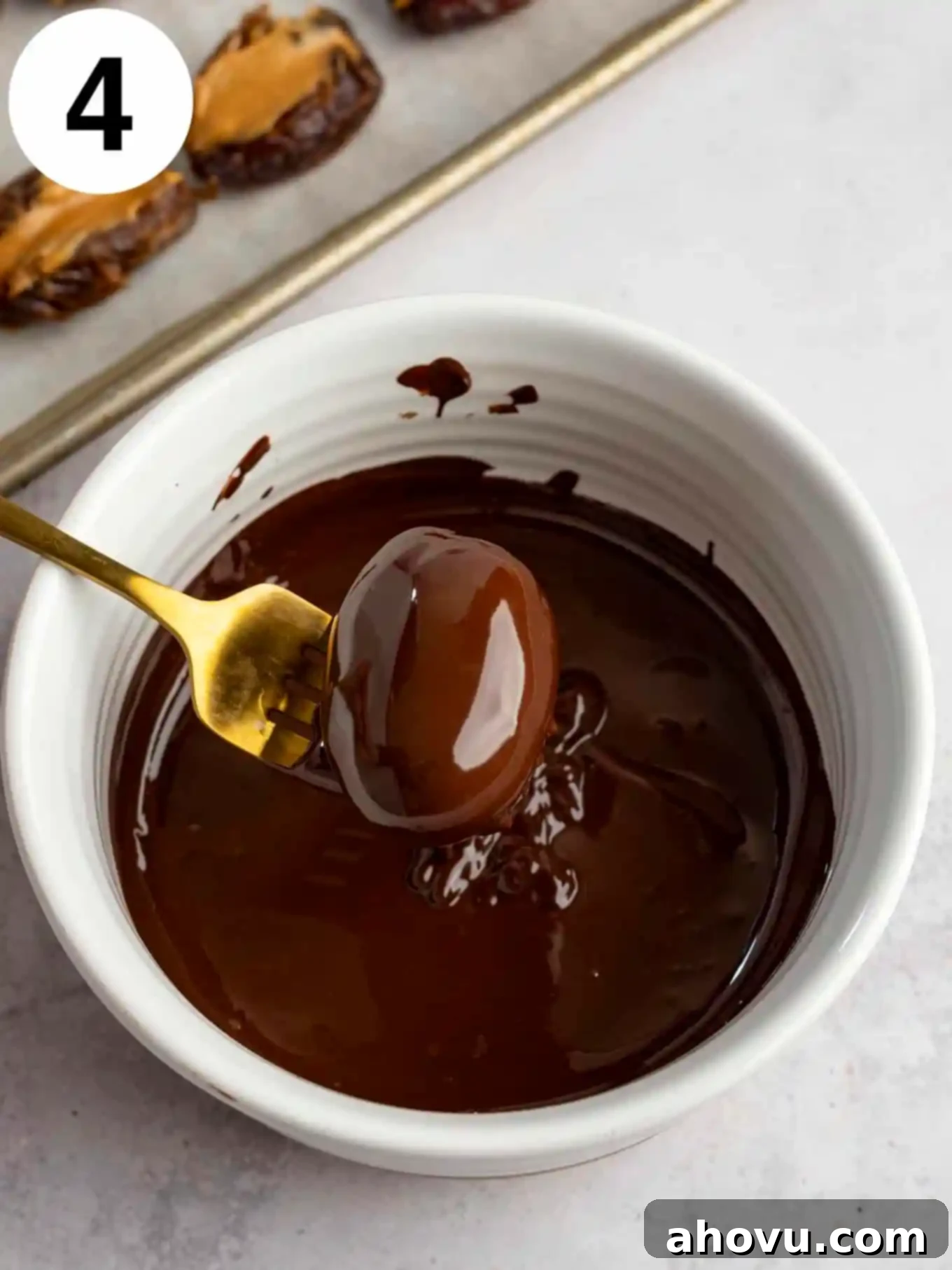 A process shot showing a date being coated in melted chocolate. 