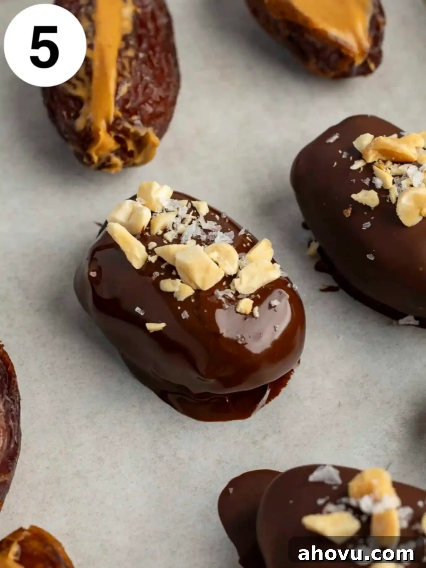 A process shot showing a chocolate coated date topped with peanuts and sea salt. 