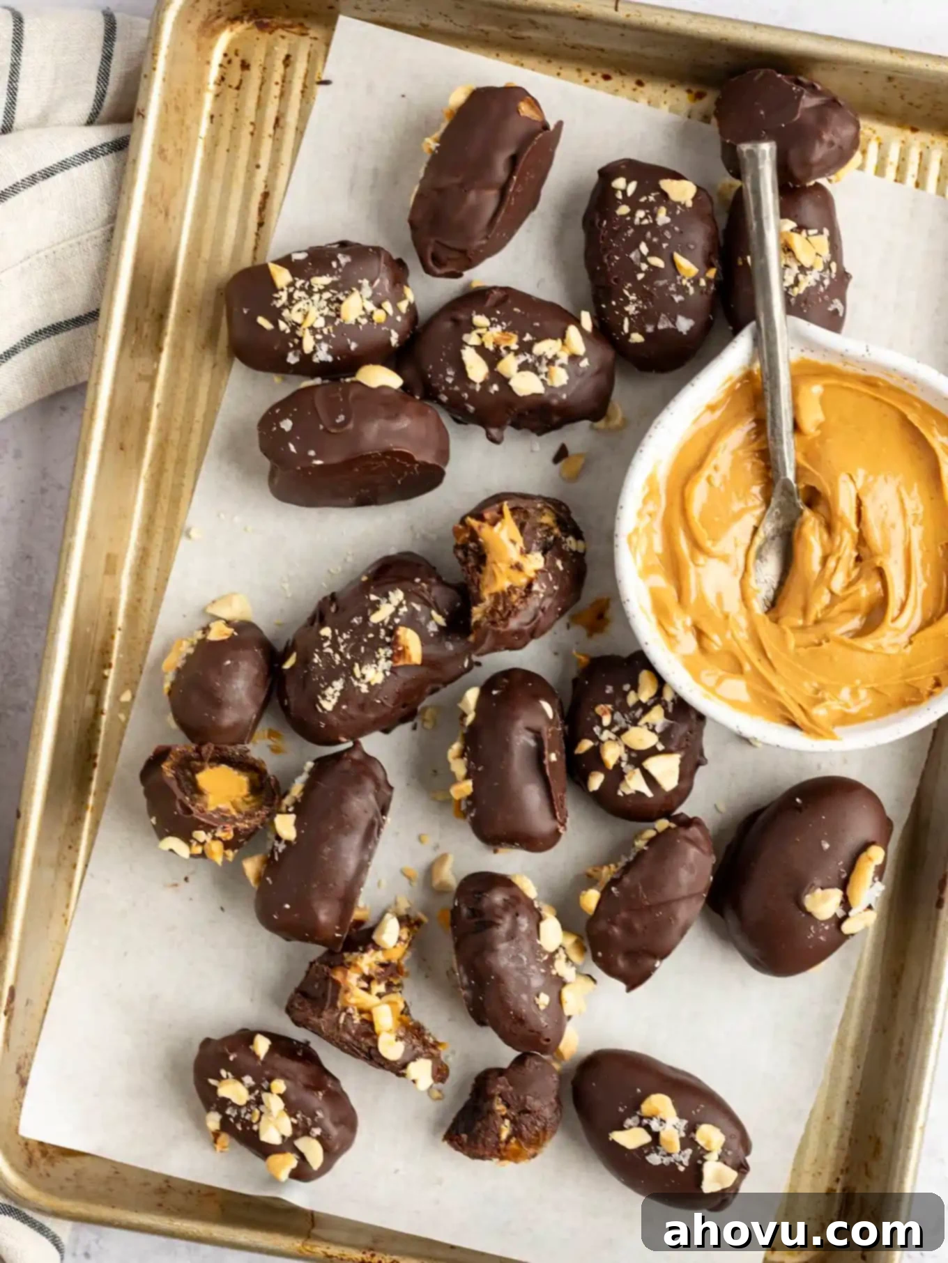 An overhead view of date Snickers arranged on a baking sheet, with a bowl of peanut butter. 