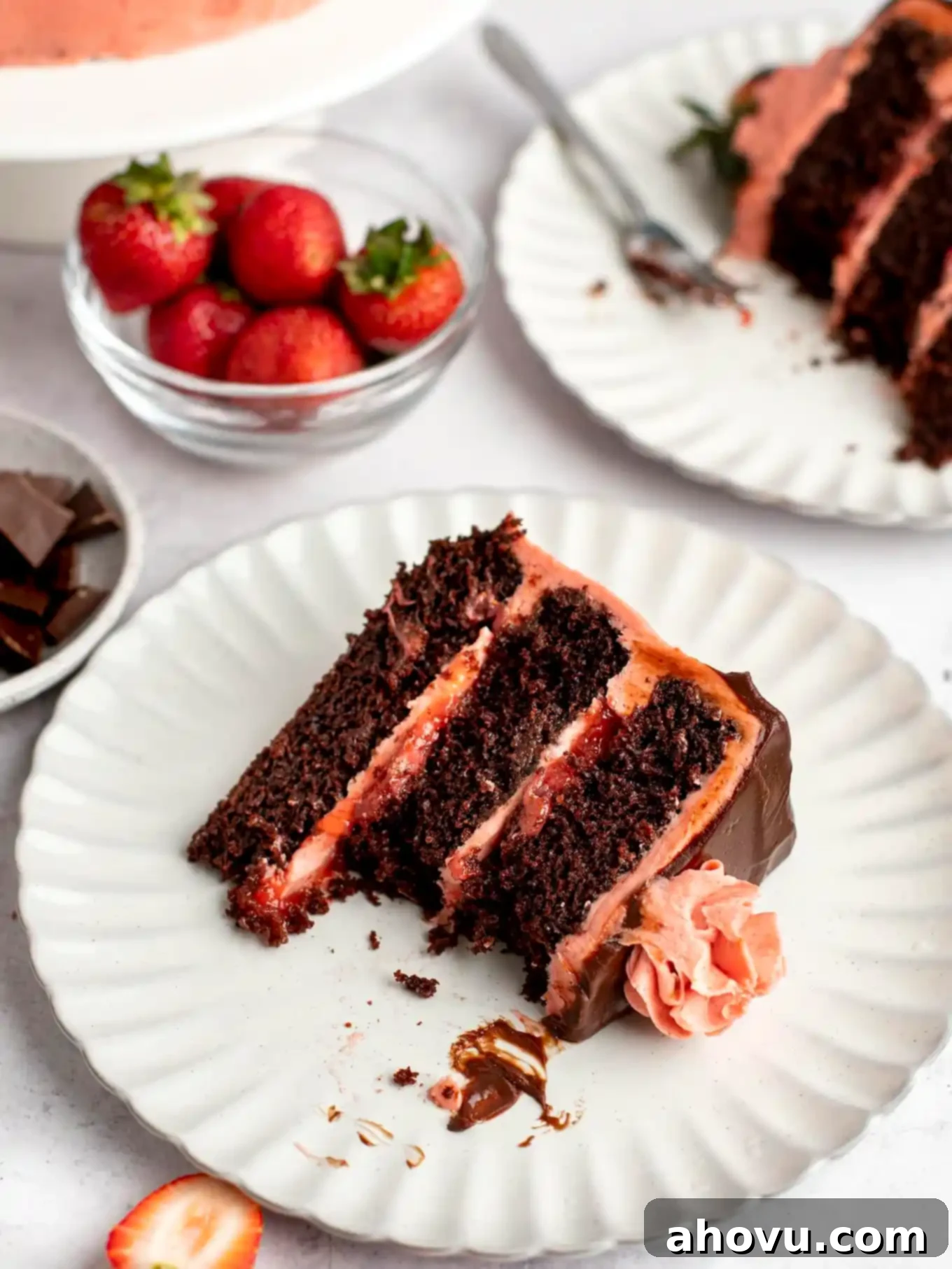 A slice of chocolate and strawberry cake on a white plate, with a bite missing. 