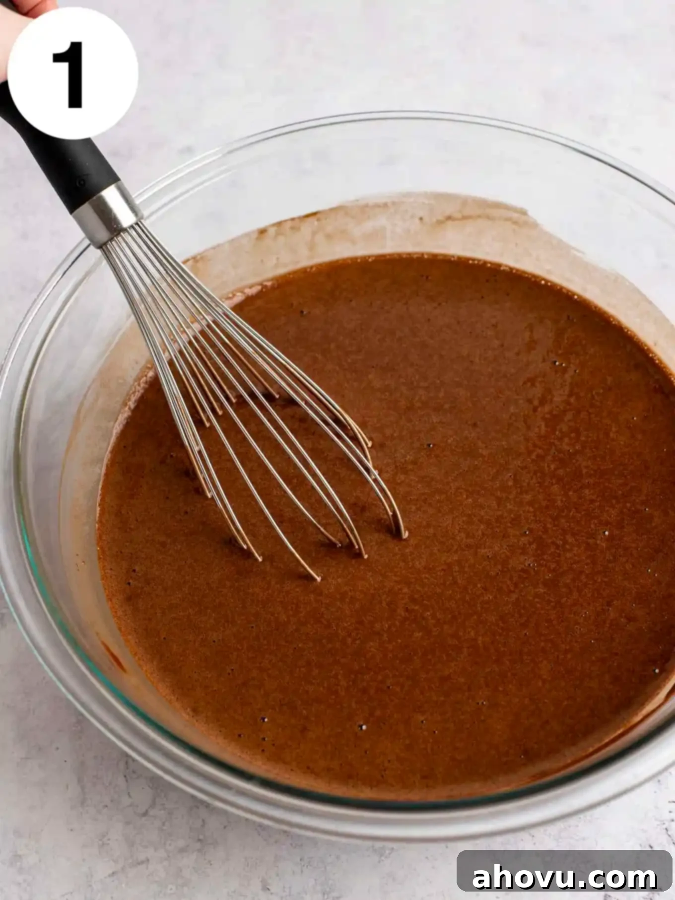 Chocolate cake batter in a glass mixing bowl, with a whisk. 