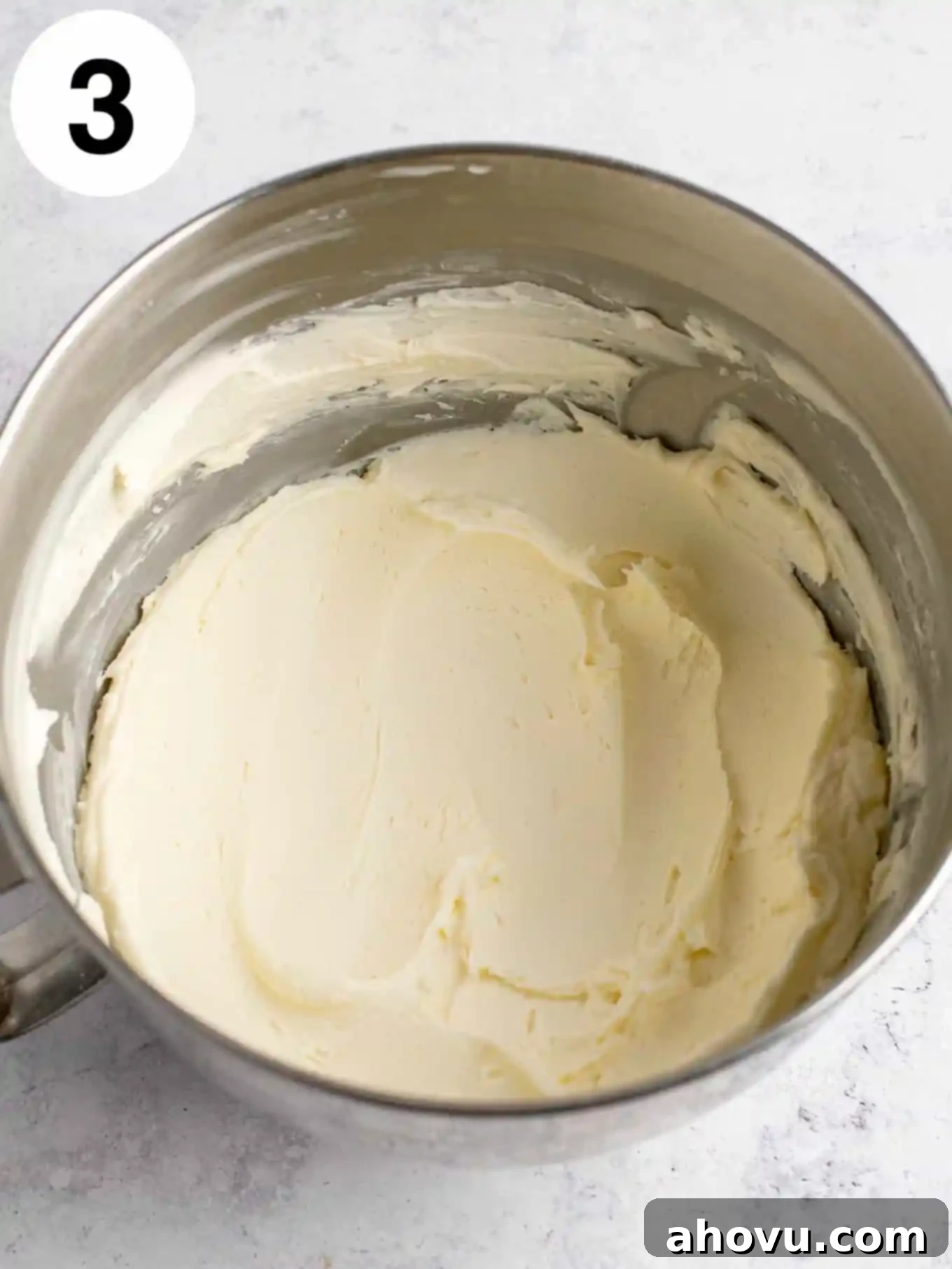 An overhead view of beaten butter and powdered sugar in a mixing bowl. 