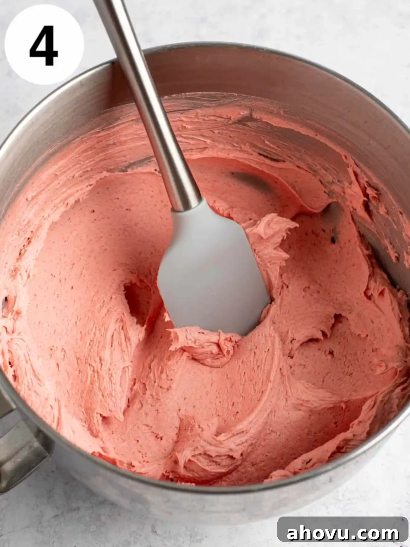 An overhead view of strawberry frosting in a mixing bowl with a spatula. 