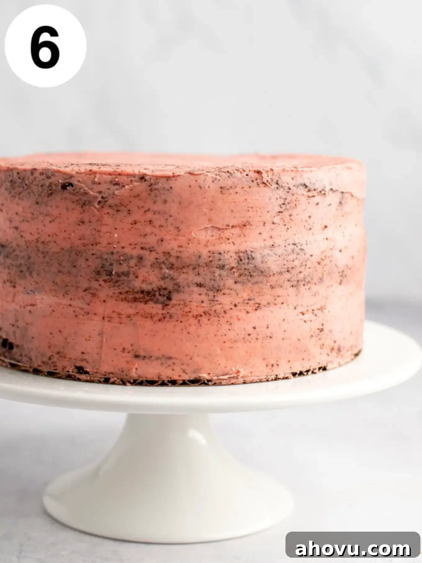 A chocolate cake on a cake stand, with a crumb coat of strawberry frosting. 