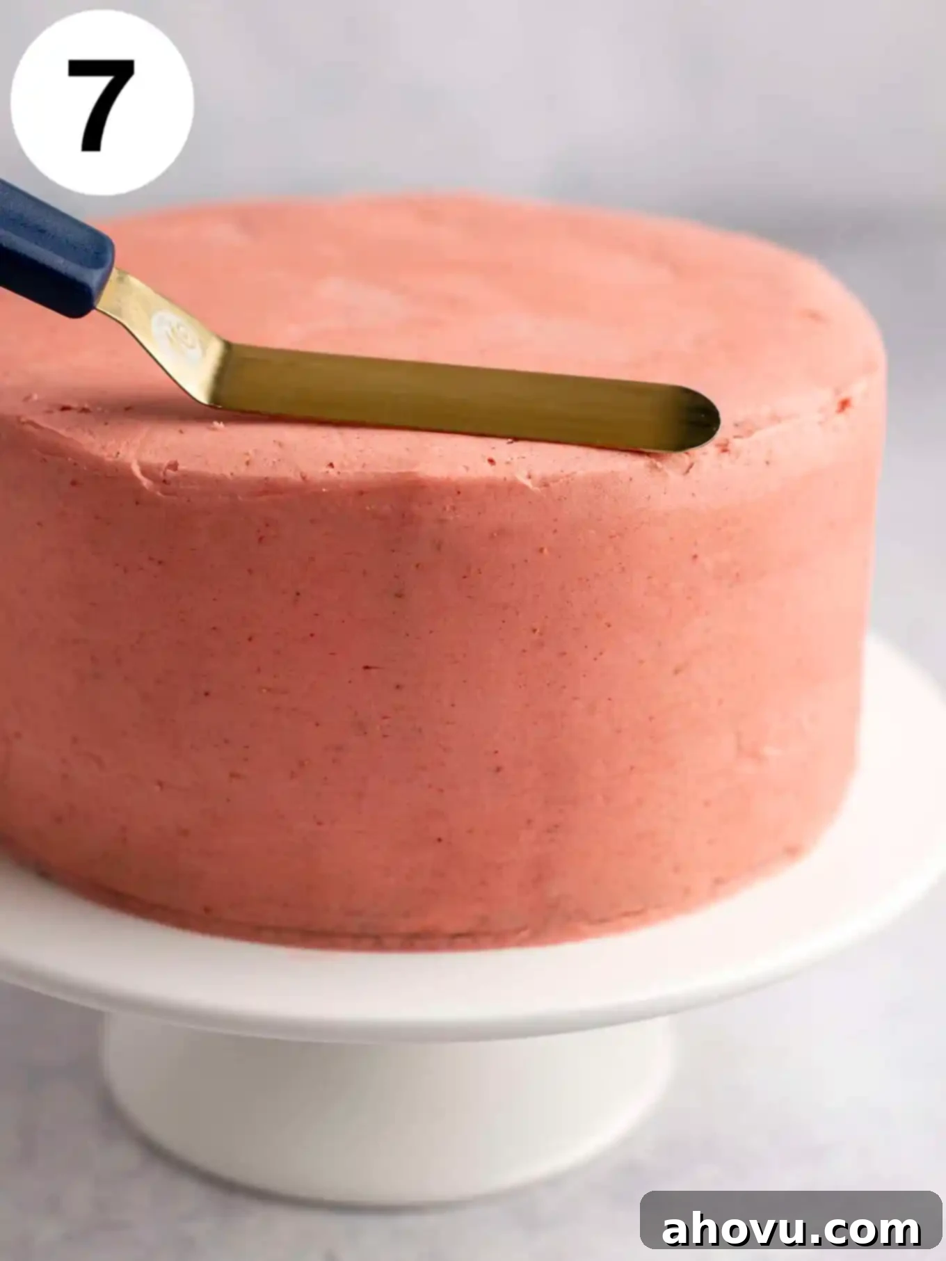 A process shot showing strawberry frosting being smoothed over a layer cake. 