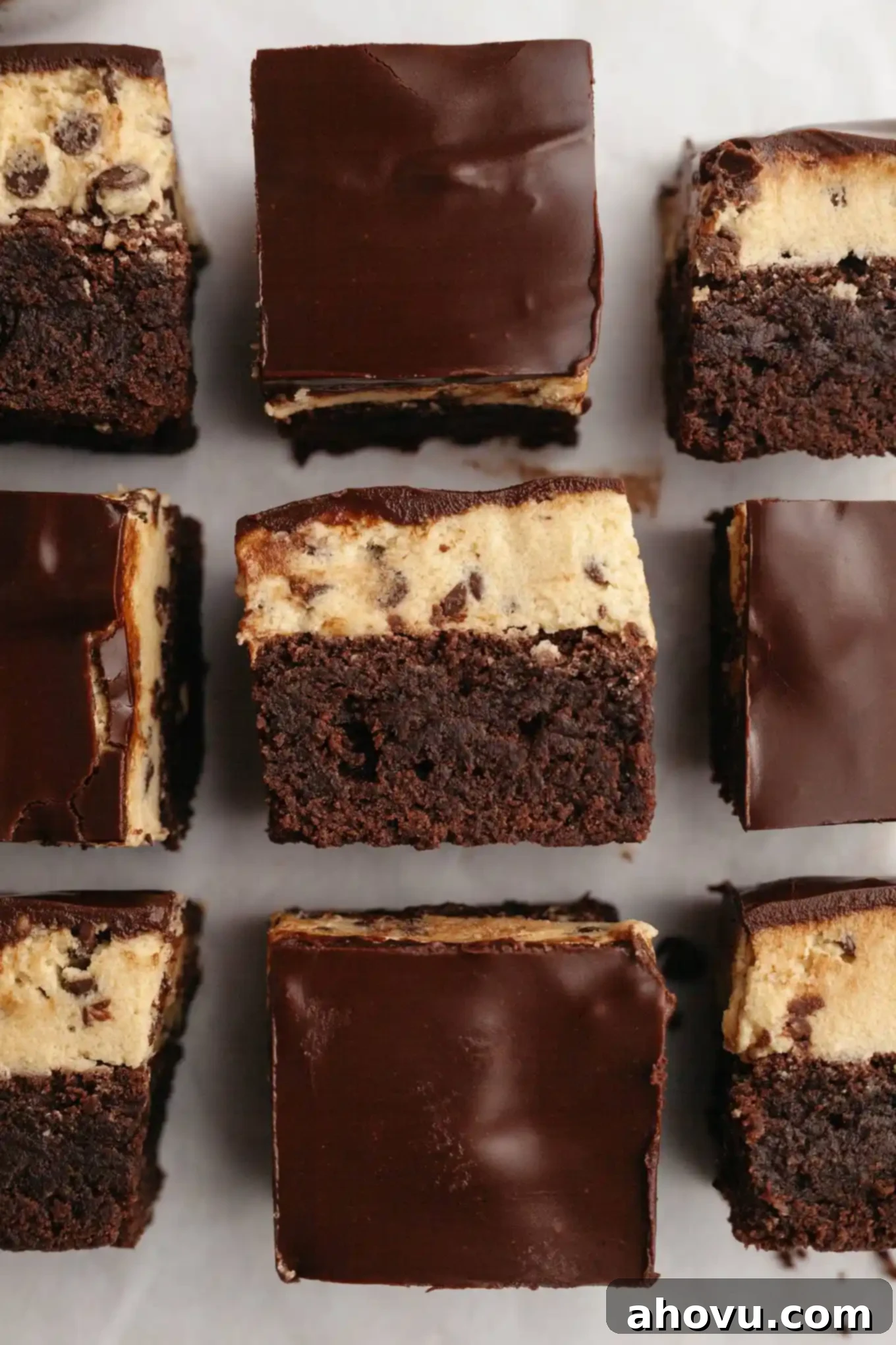 An overhead view of sliced cookie dough brownies, some of which are turned on their sides, showcasing the distinct layers of fudgy brownie, creamy cookie dough, and glossy chocolate topping.