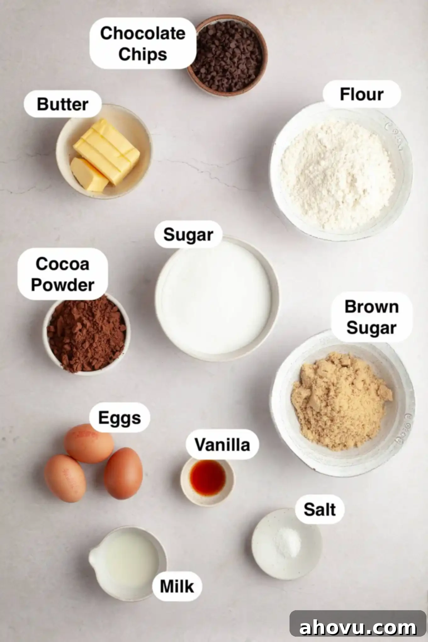 An overhead view of the carefully measured ingredients for making cookie dough brownies, including cocoa powder, butter, sugars, flour, and chocolate chips, ready for preparation.