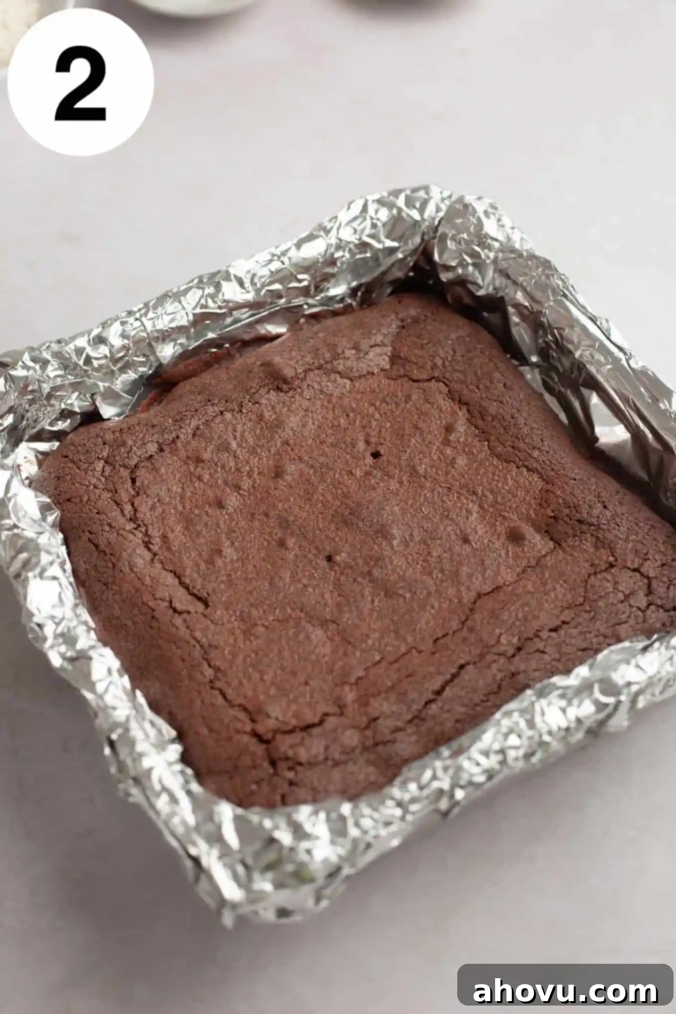 Freshly baked chocolate brownies cooling in a foil-lined square pan, their tops crinkly and set.