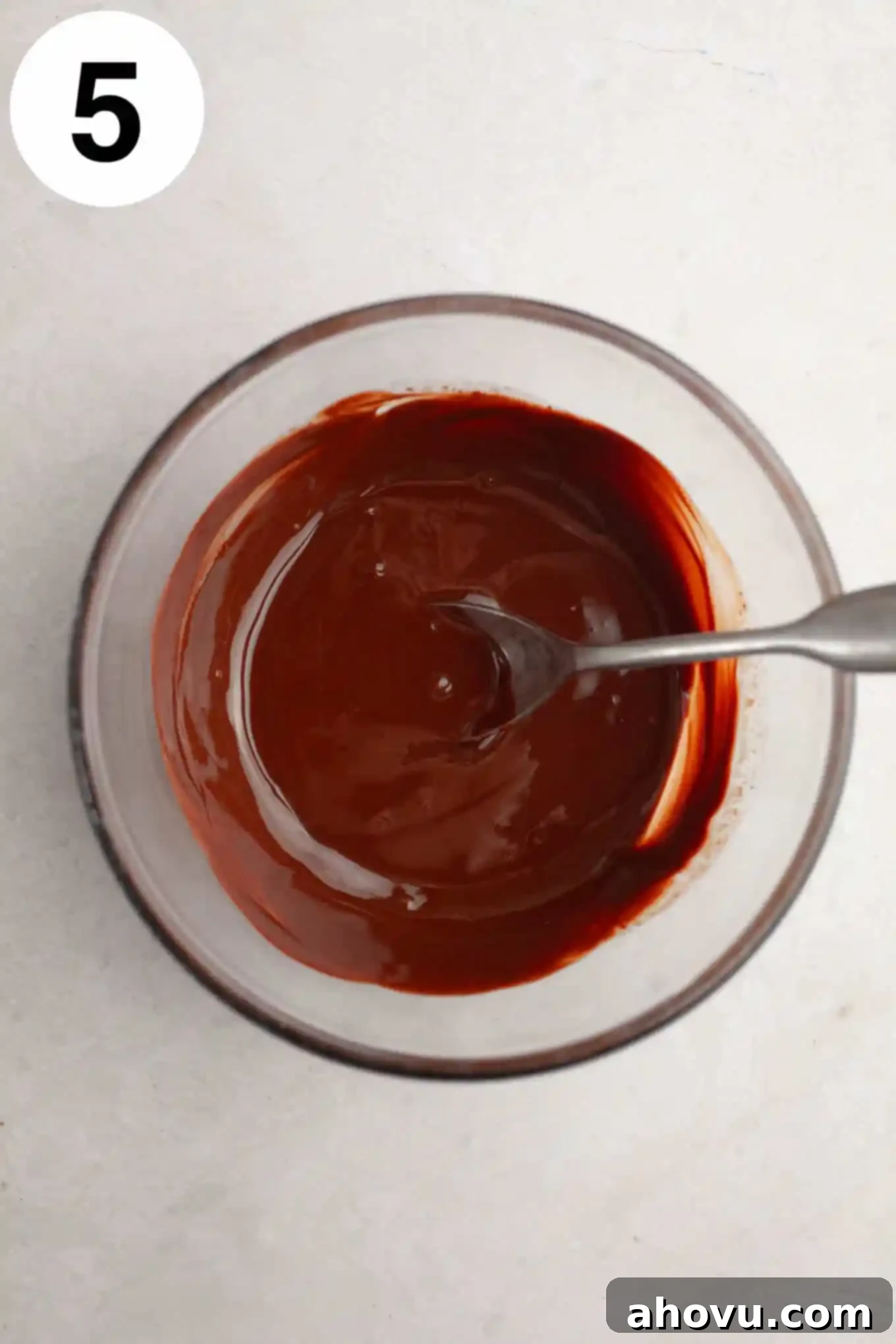 An overhead view of melted chocolate in a clear glass bowl, smooth and glossy, ready for pouring.