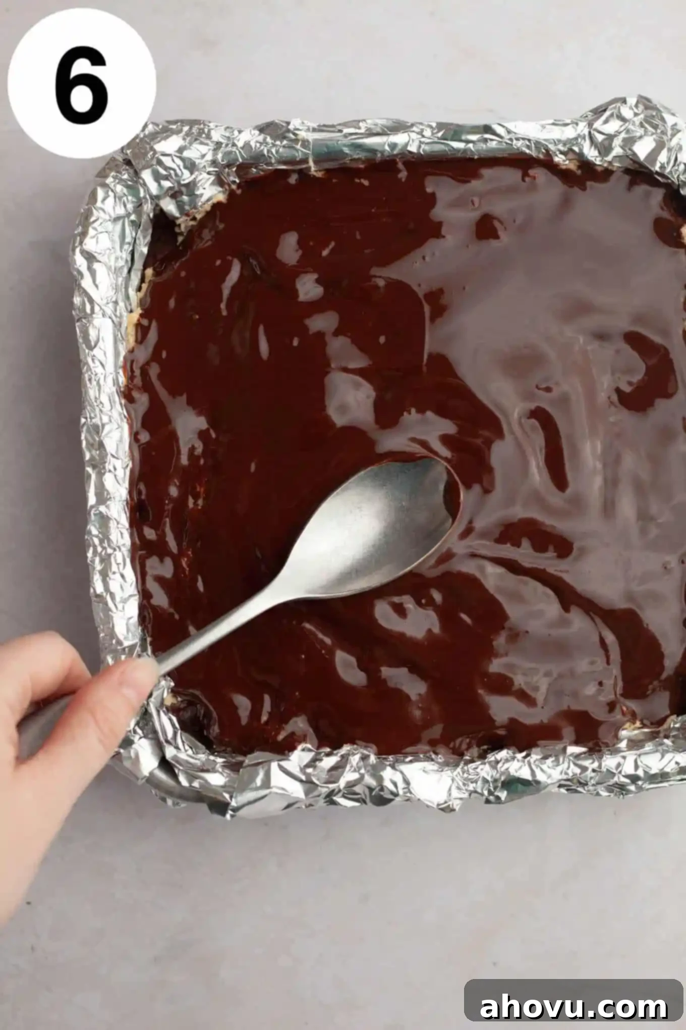 An overhead view of luscious melted chocolate being spread over the cookie dough layer of the brownies, creating a smooth, even topping.