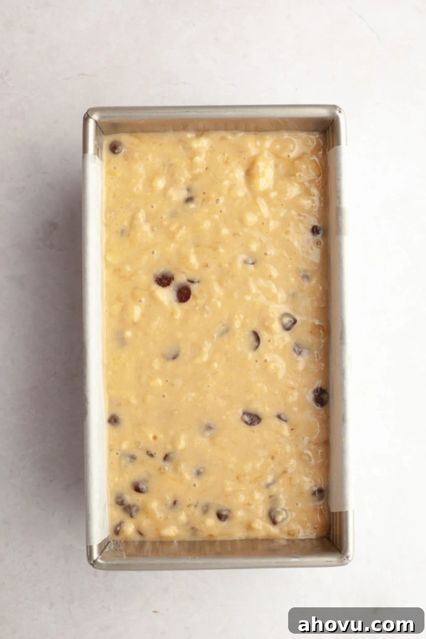 A loaf pan lined with parchment paper, with banana bread batter inside, ready for baking.