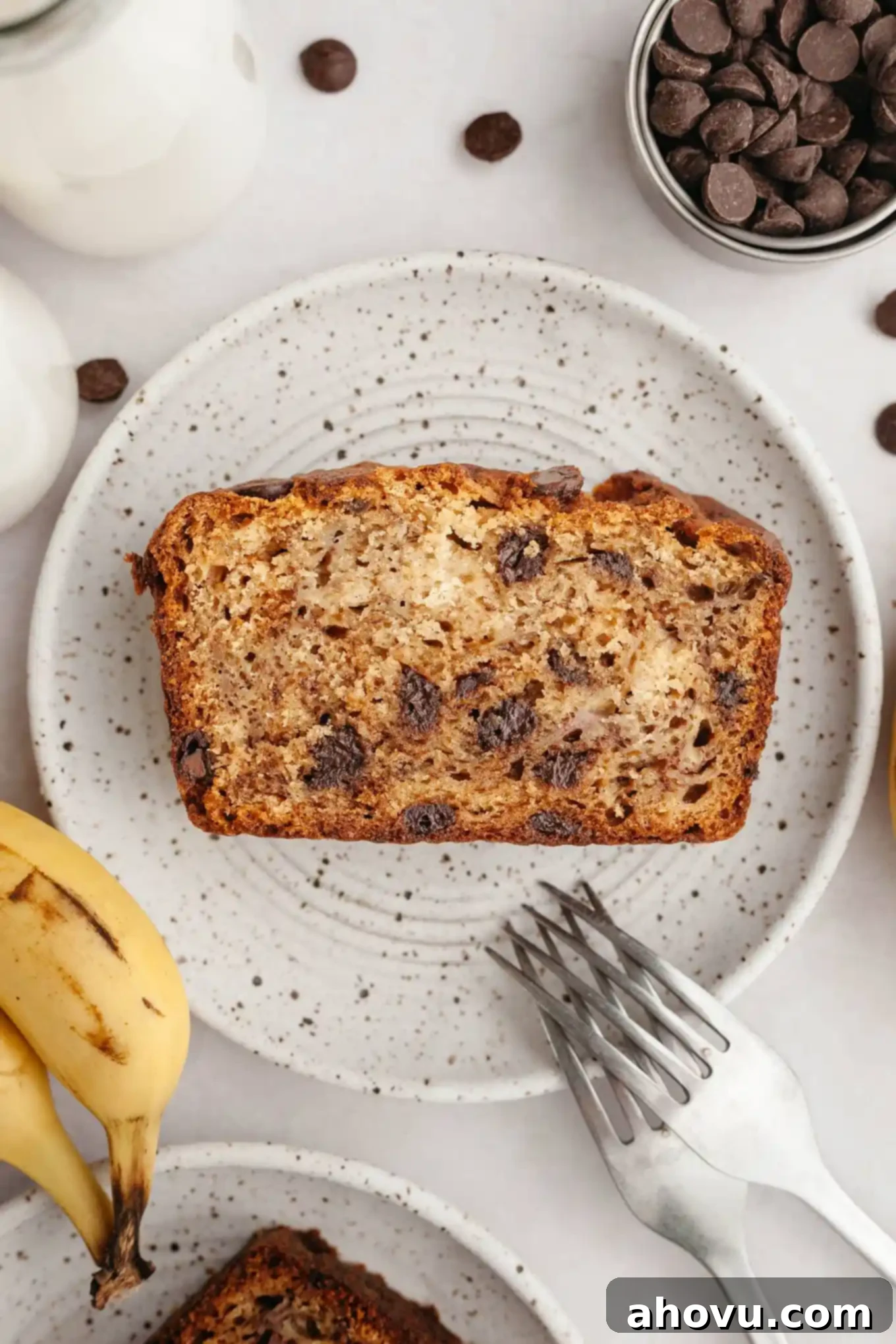 An overhead view of a perfectly baked slice of chocolate chip banana bread on a speckled plate.