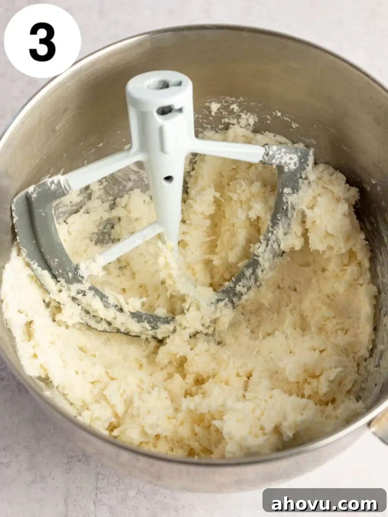 An overhead view of a mixing bowl containing butter, cream cheese, powdered sugar, and shredded coconut, ready to be combined.