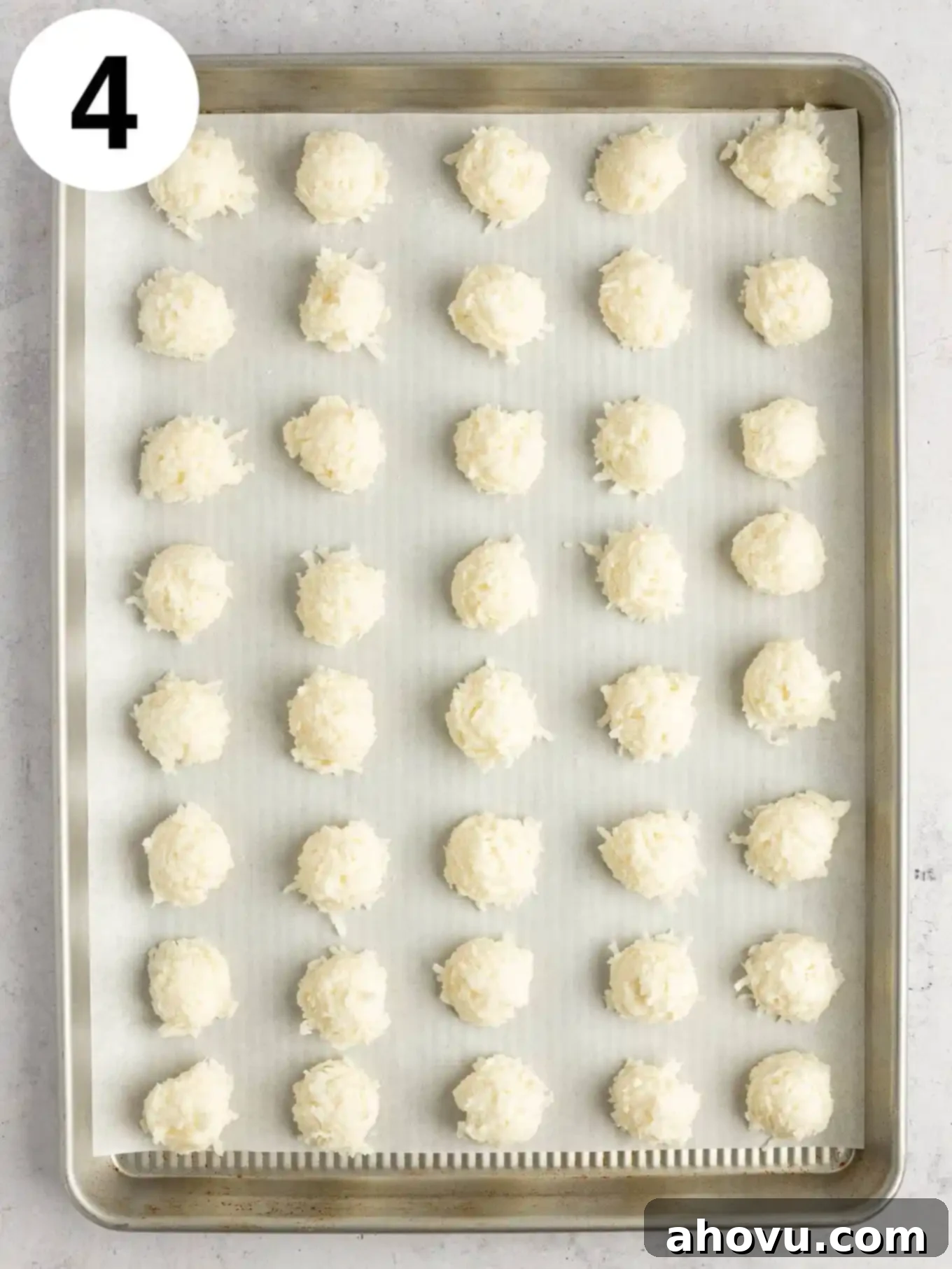 An overhead process shot showing small balls of the creamy coconut mixture placed on a parchment-lined baking sheet, waiting to be shaped.