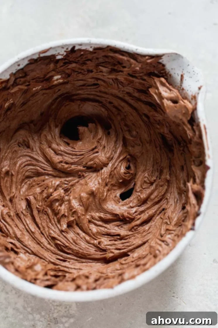 A mixing bowl filled with rich chocolate ganache that has been expertly whipped, showcasing a lightened, fluffy texture perfect for frosting.