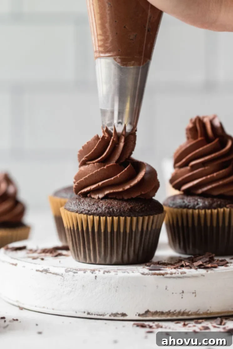 A rustic white board showcasing decadent chocolate cupcakes topped with generous swirls of fluffy, whipped chocolate ganache frosting, ready for serving.