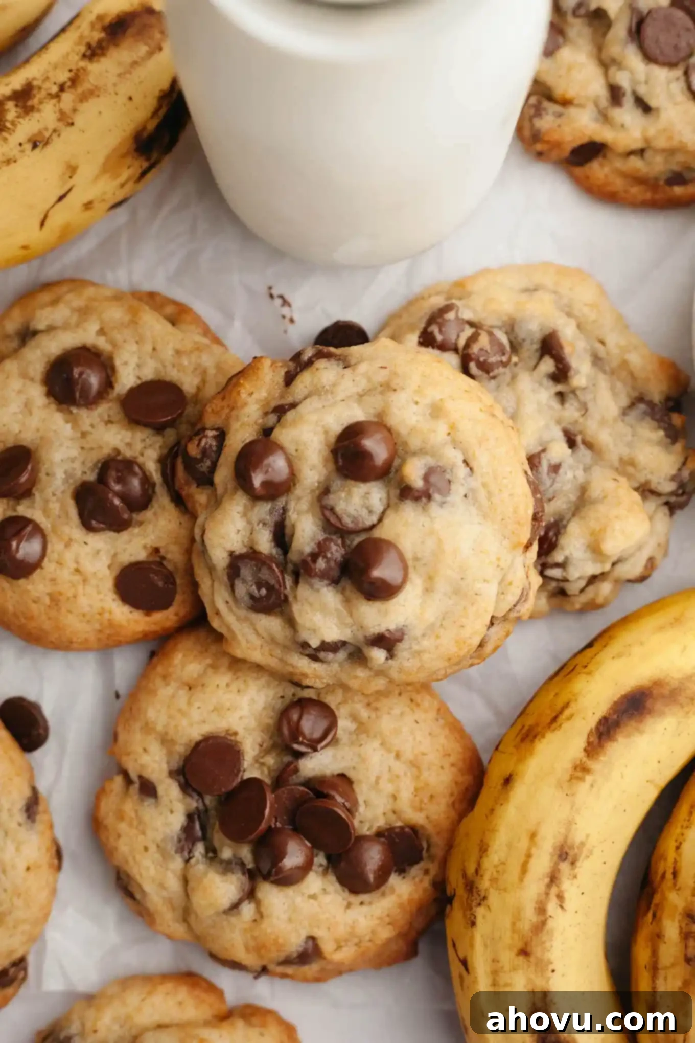 Irresistible Banana Chocolate Chip Cookies 7 An overhead view of freshly baked banana chocolate chip cookies next to a bunch of ripe bananas on a wooden surface.