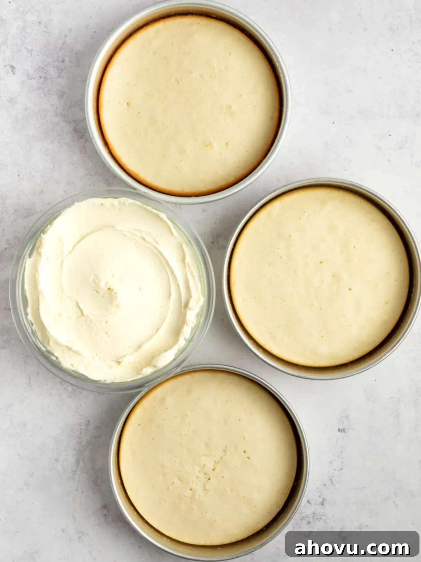 An overhead view of three baked cake layers and a bowl of frosting. 