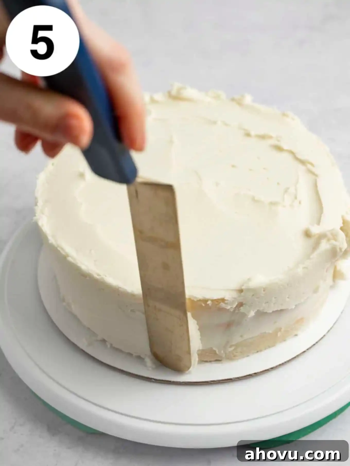 A process shot showing frosting being spread over a layer cake with an offset spatula. 