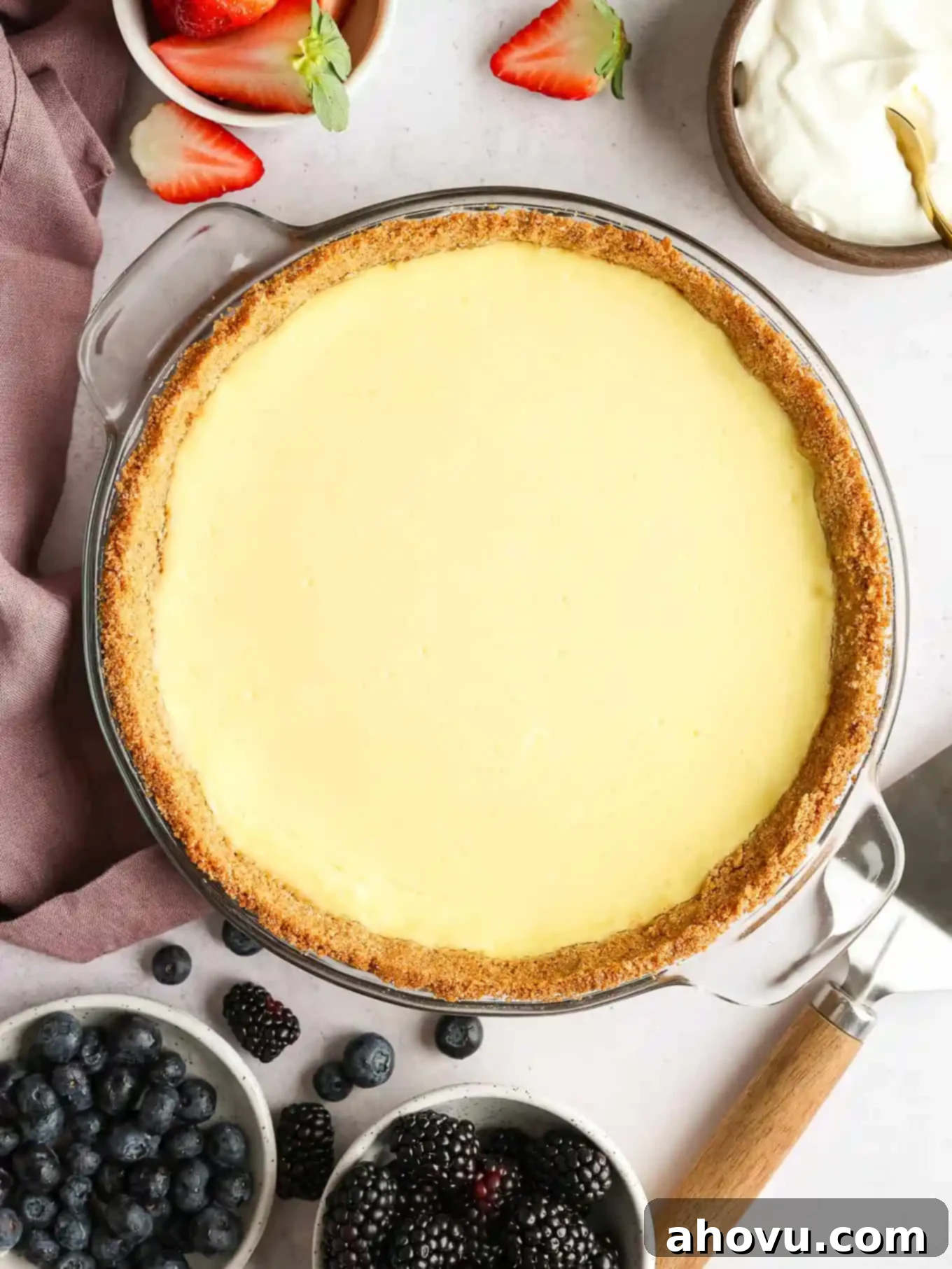 Overhead view of an unsliced cheesecake pie, surrounded by berries. 