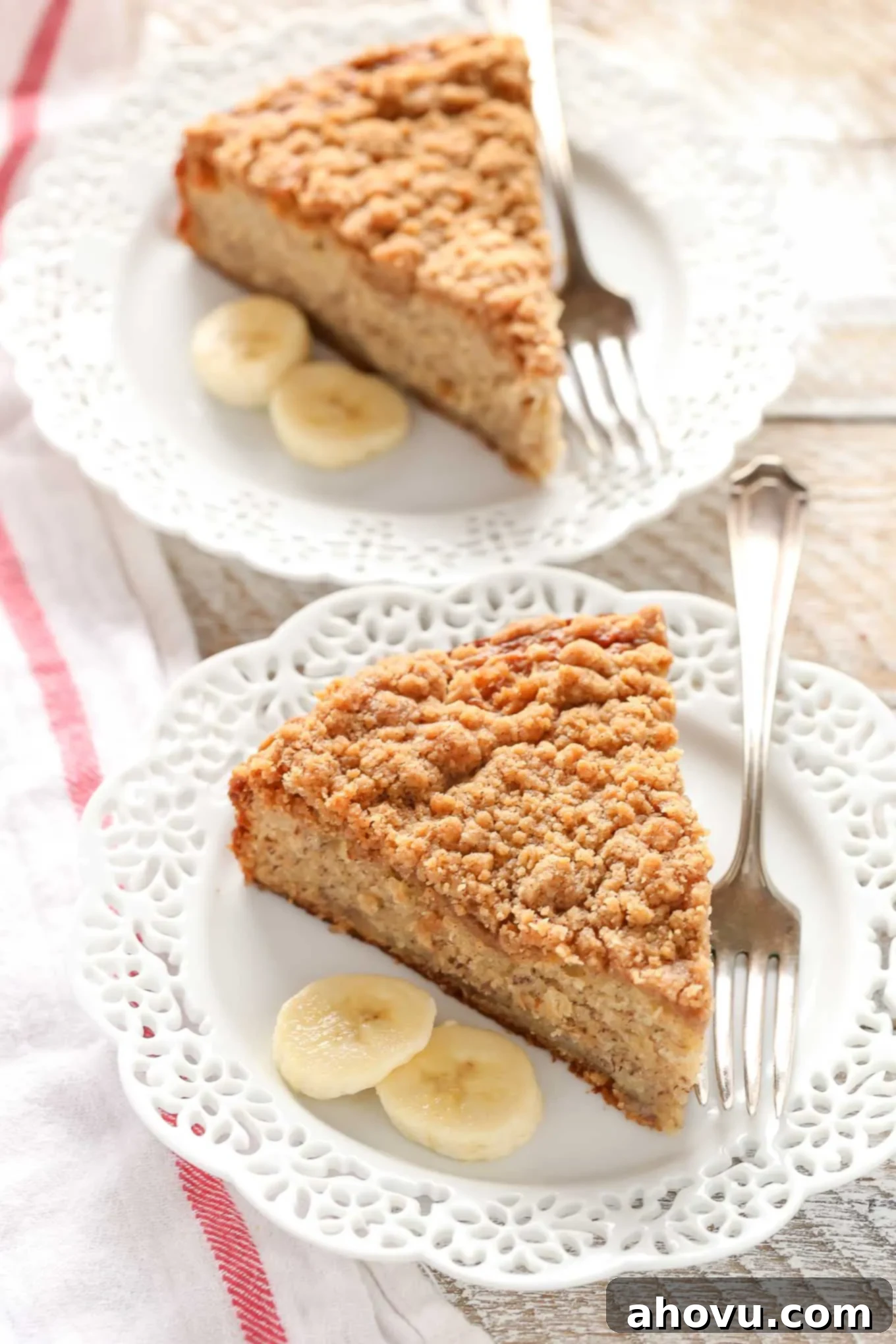 Two slices of banana cake with buttermilk on white plates. Forks and banana slices are also on the plates. 