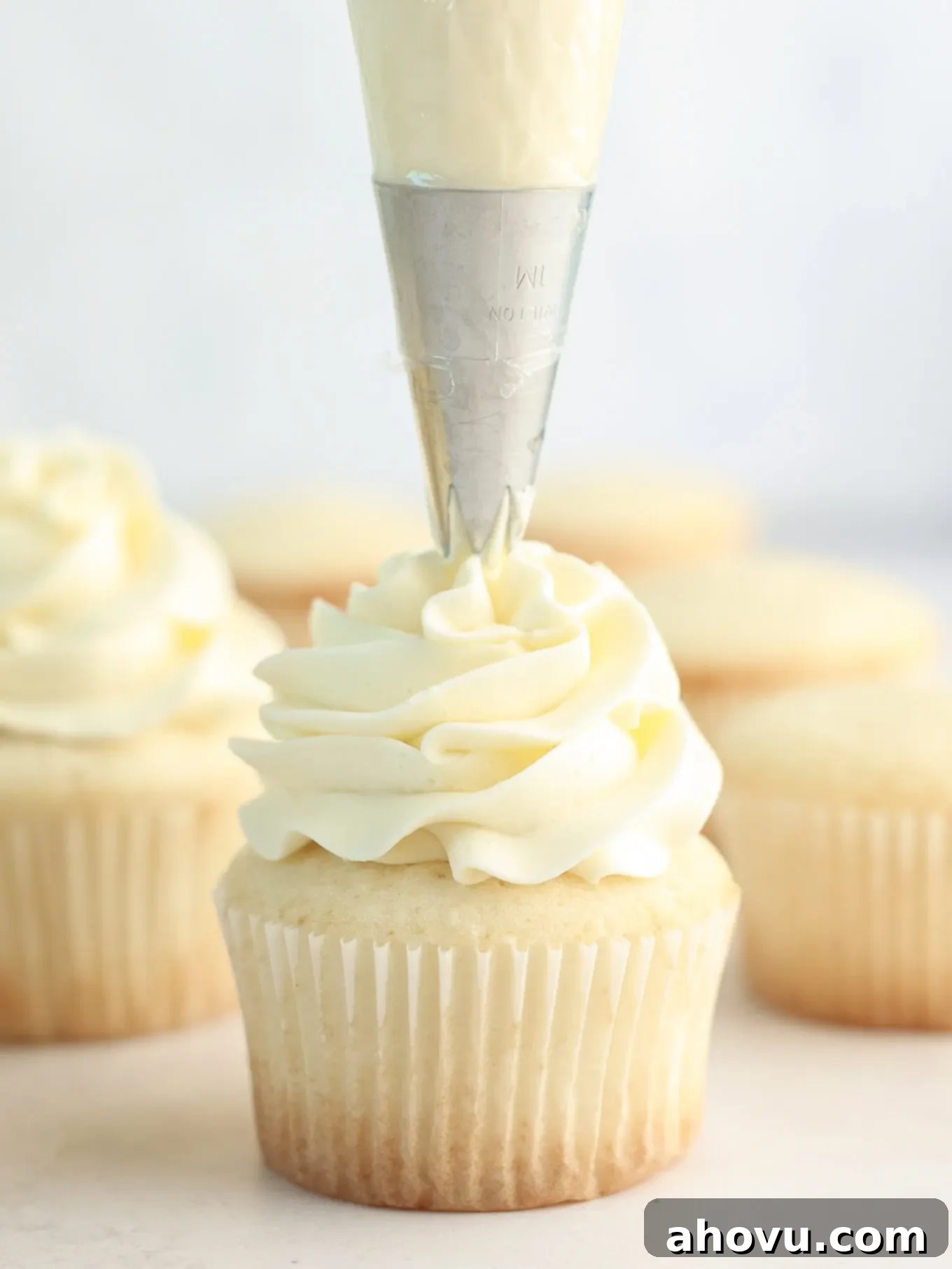 Vanilla frosting being expertly piped onto a freshly baked white cupcake, ready for serving.