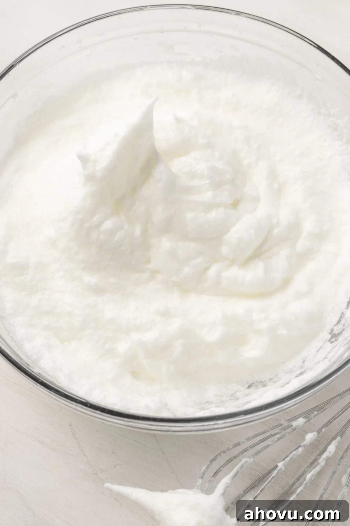 A clear glass mixing bowl filled with egg whites that have been perfectly beaten to stiff peaks, standing tall and firm.