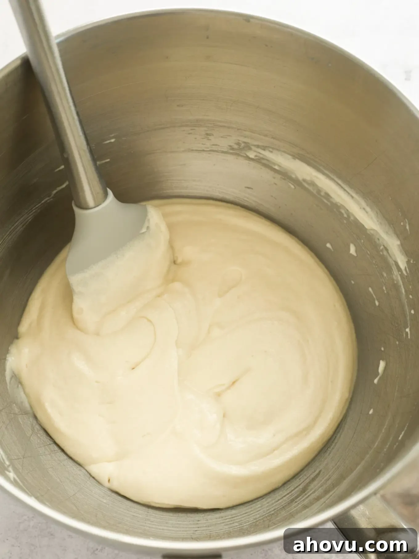 White cupcake batter in a mixing bowl, showing the light and airy texture after egg whites have been folded in, with a rubber spatula resting inside.