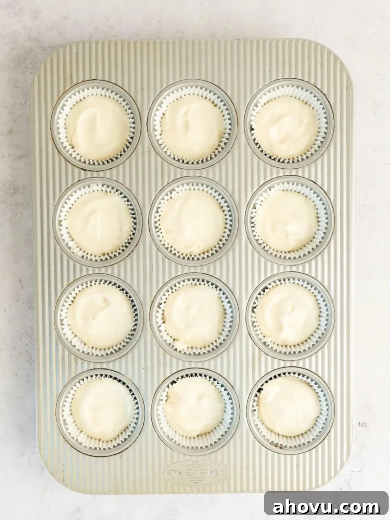 Overhead view of cupcake liners neatly filled with white cupcake batter, ready for baking.