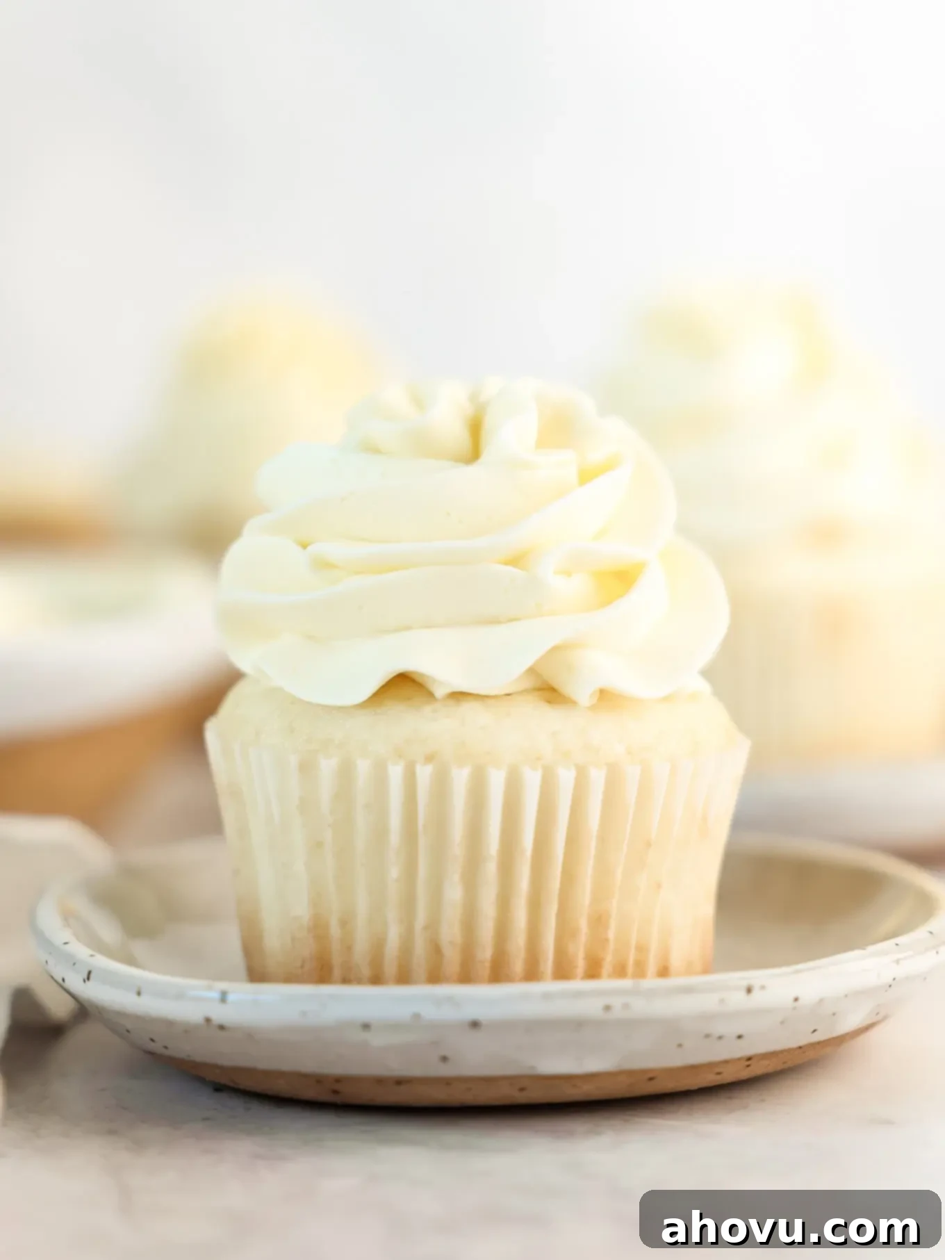 A perfectly baked and frosted white cupcake presented on a white plate, showcasing its soft crumb.