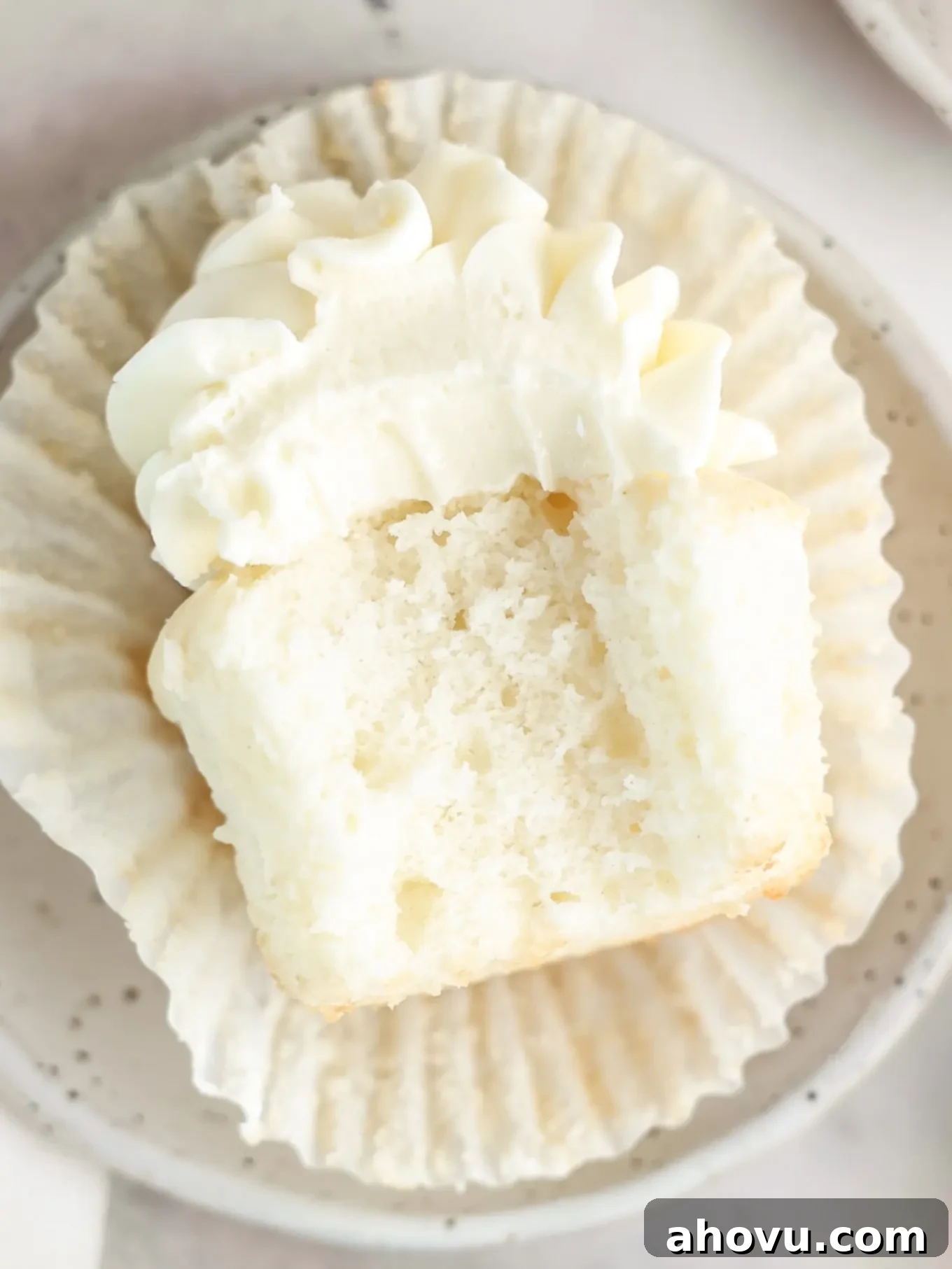 A delicious white cupcake on its side with a bite taken out, revealing its perfectly moist and fluffy interior.