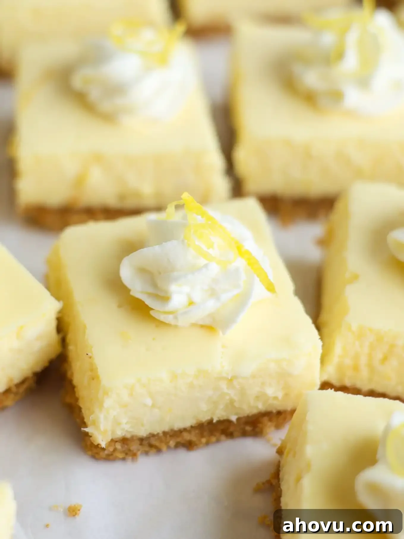 Beautifully sliced lemon cheesecake bars, artfully topped with fluffy whipped cream, ready to serve.