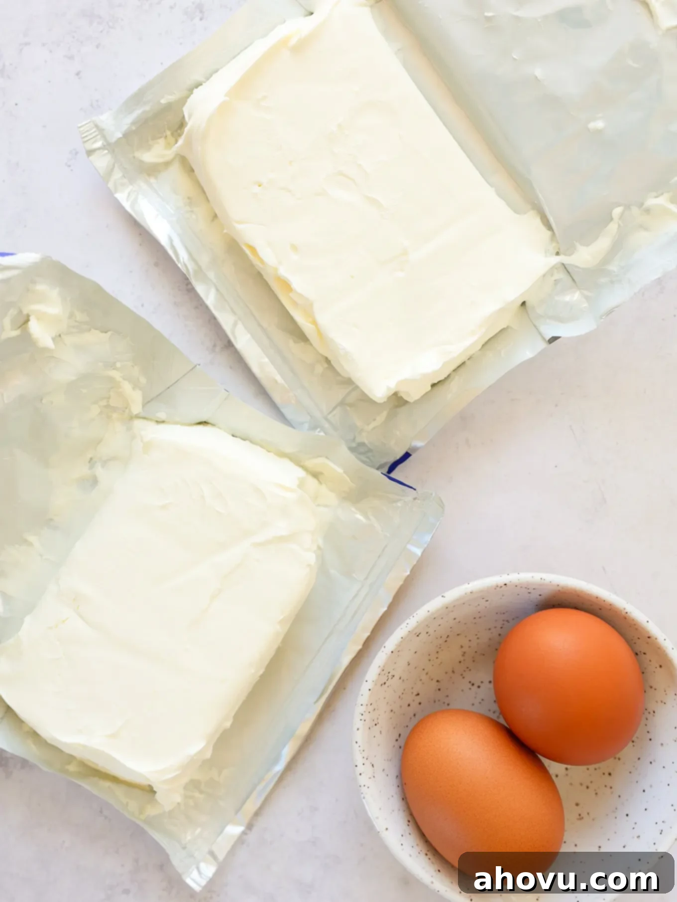 Overhead view of blocks of cream cheese and fresh eggs, ready for baking.