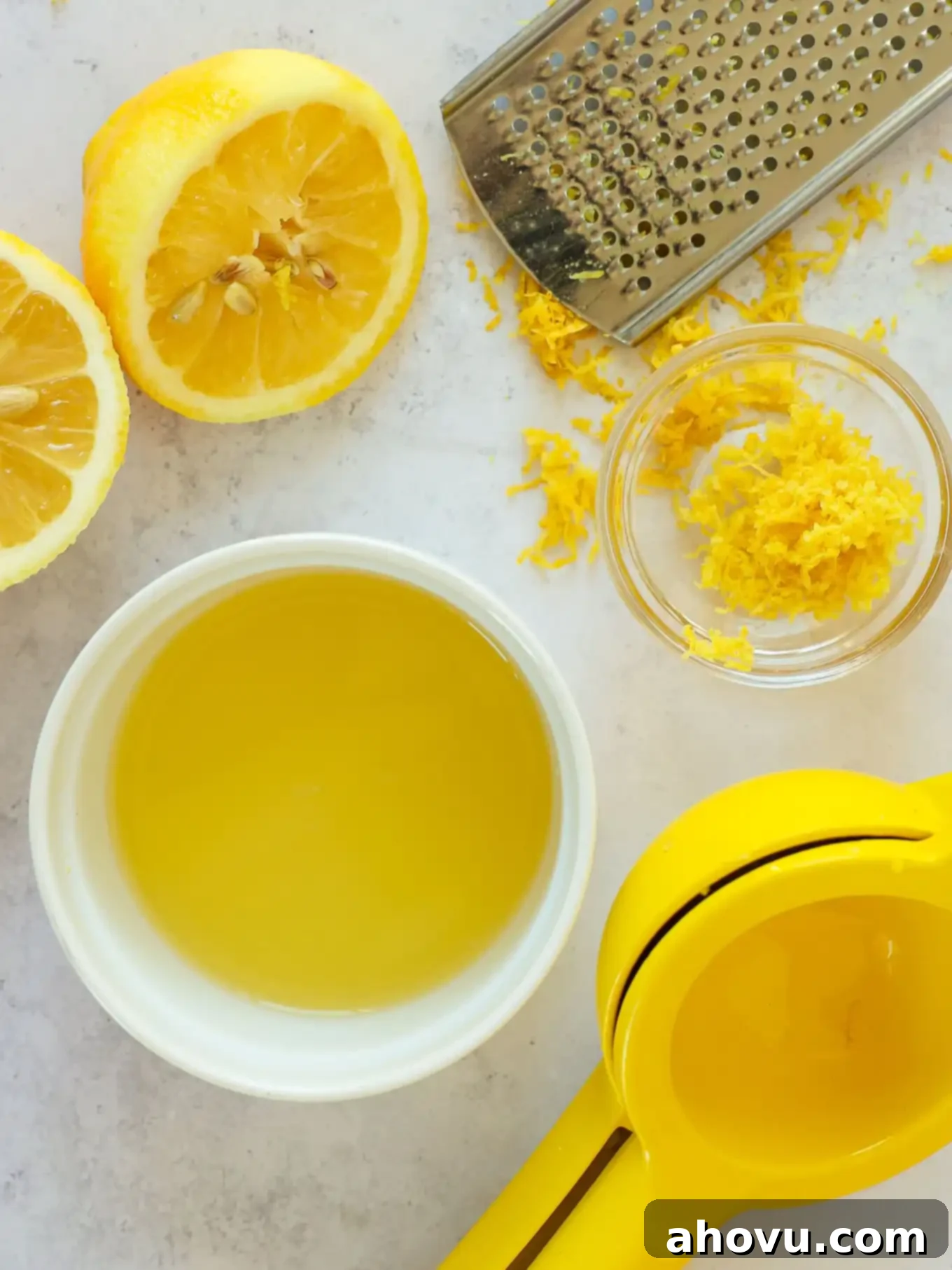 An overhead view of halved lemons, a bowl of fresh lemon juice, and finely grated lemon zest.