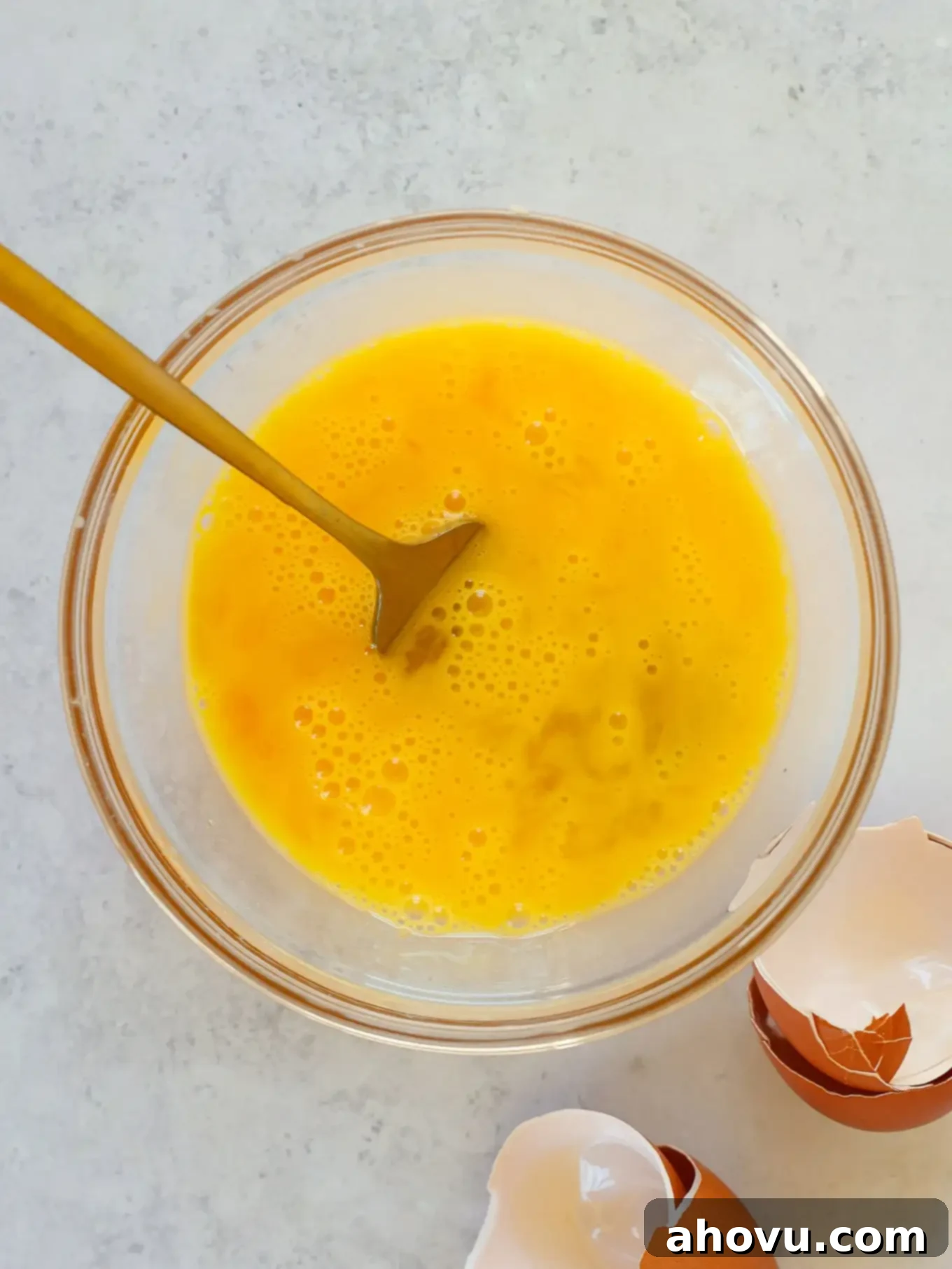 An overhead view of lightly beaten eggs in a glass bowl, ready to be incorporated into the cheesecake batter.