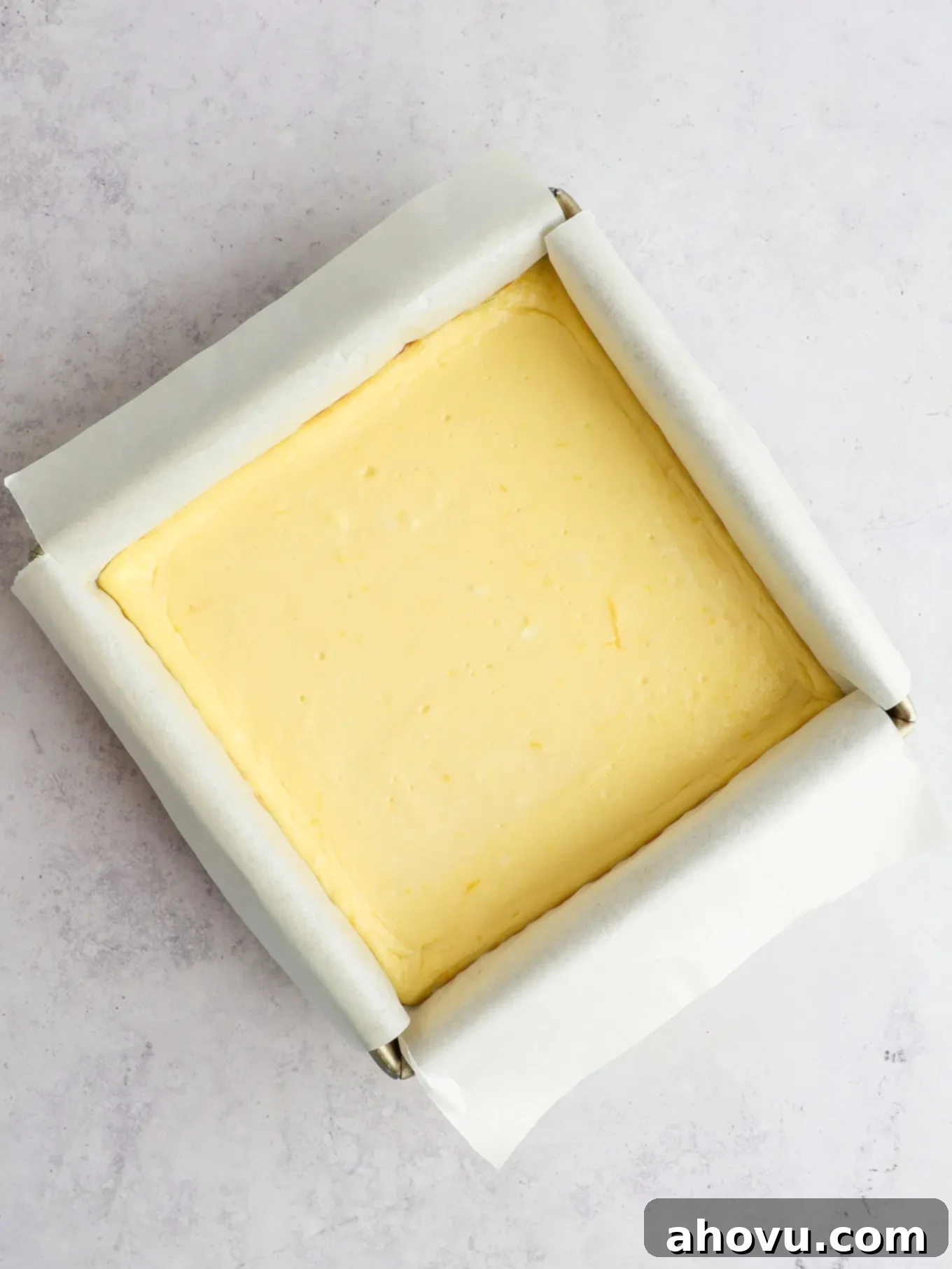 An overhead view of baked lemon cheesecake bars in a baking pan, showing a smooth, crack-free surface.