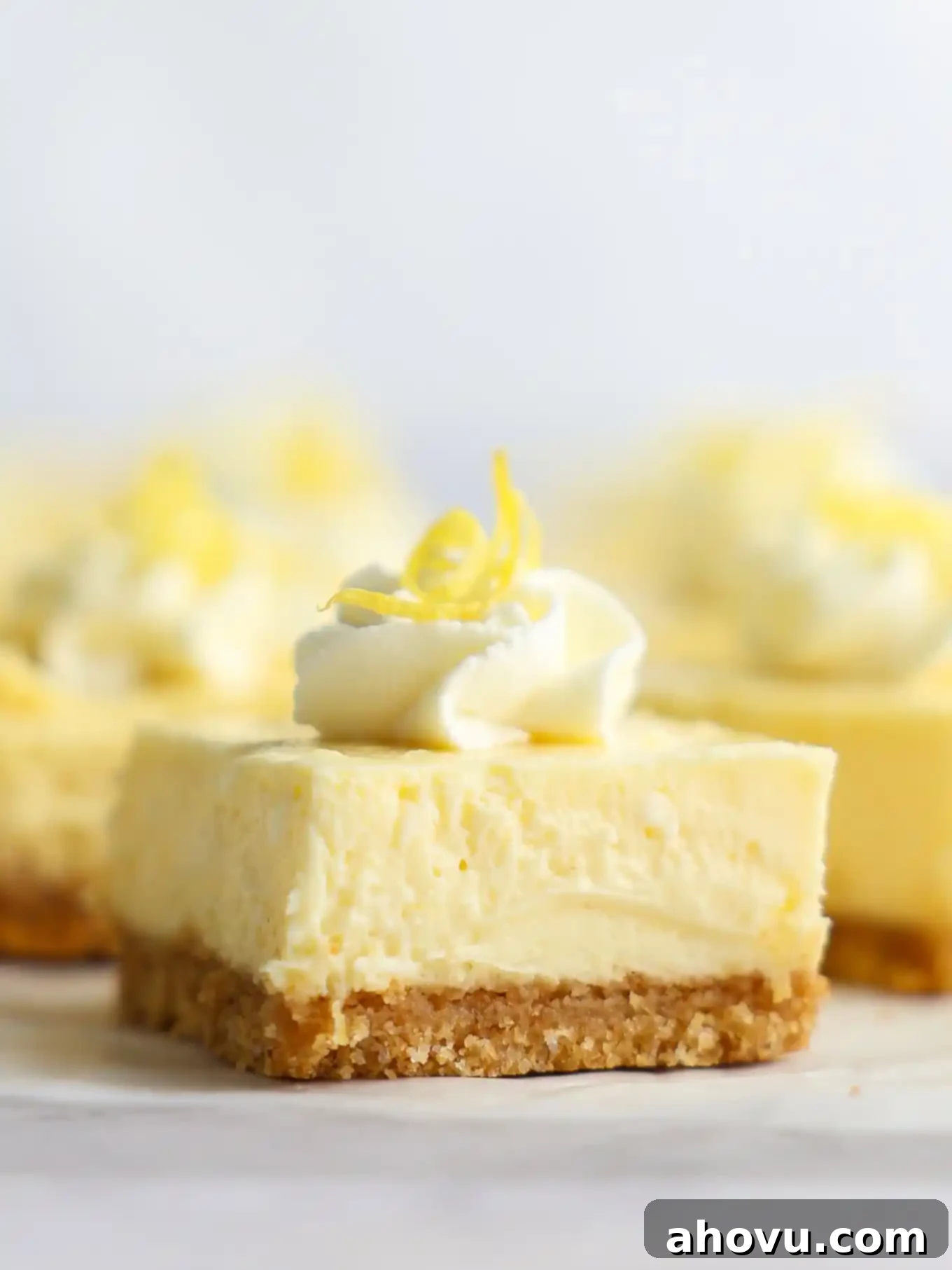 A close-up view of a single lemon cheesecake bar, showcasing its thick, creamy filling and golden crust.