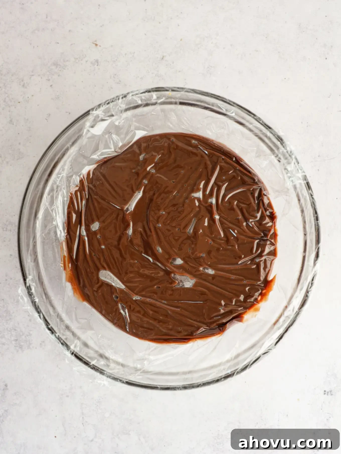 Chocolate gravy in a glass bowl with plastic wrap on top.