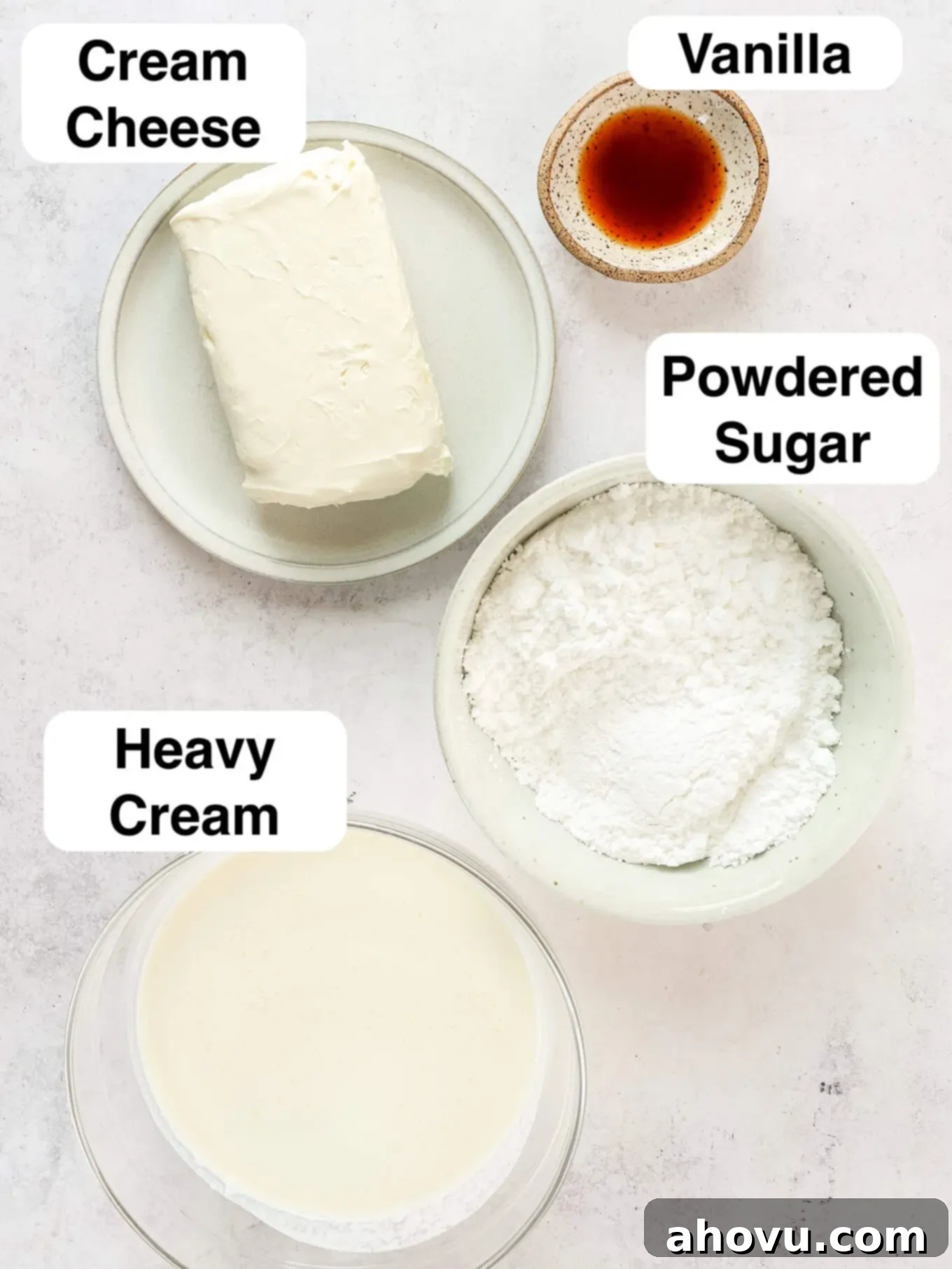 A clean, organized overhead shot of the four key ingredients required for making whipped cream cheese frosting: cream cheese, powdered sugar, vanilla extract, and heavy whipping cream.