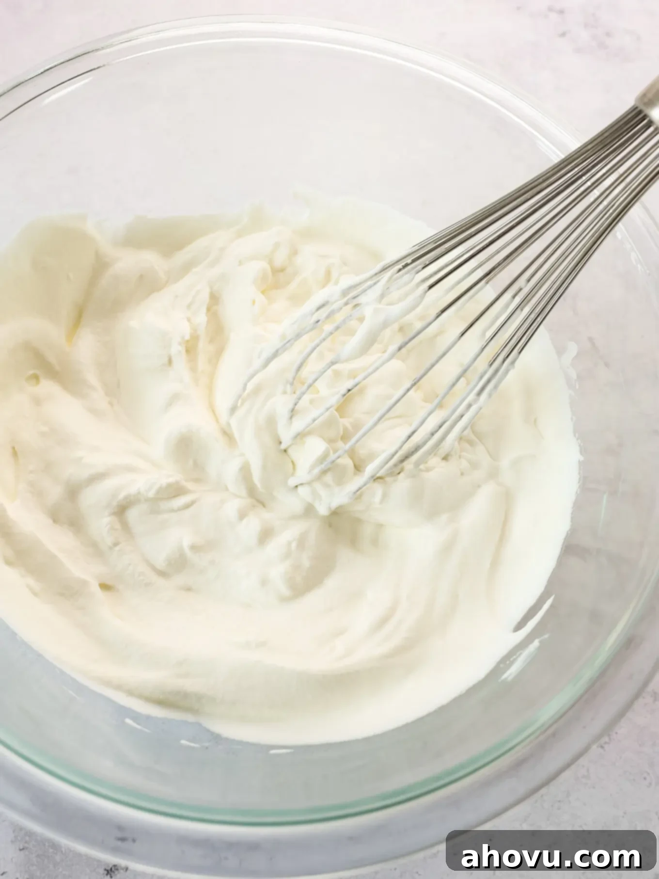 A bowl of freshly whipped heavy cream with a whisk resting in it, highlighting the stiff peaks achieved through proper beating.