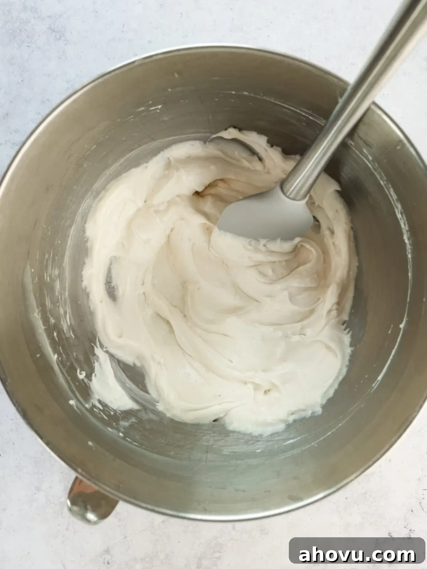Overhead view of a smooth, beaten cream cheese mixture in a mixing bowl with a spatula, ready for the whipped cream.