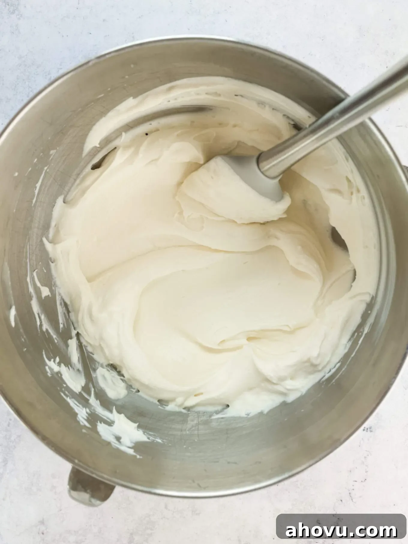 Overhead view of the finished whipped cream cheese frosting in a bowl with a spatula, showcasing its fluffy and uniform texture.