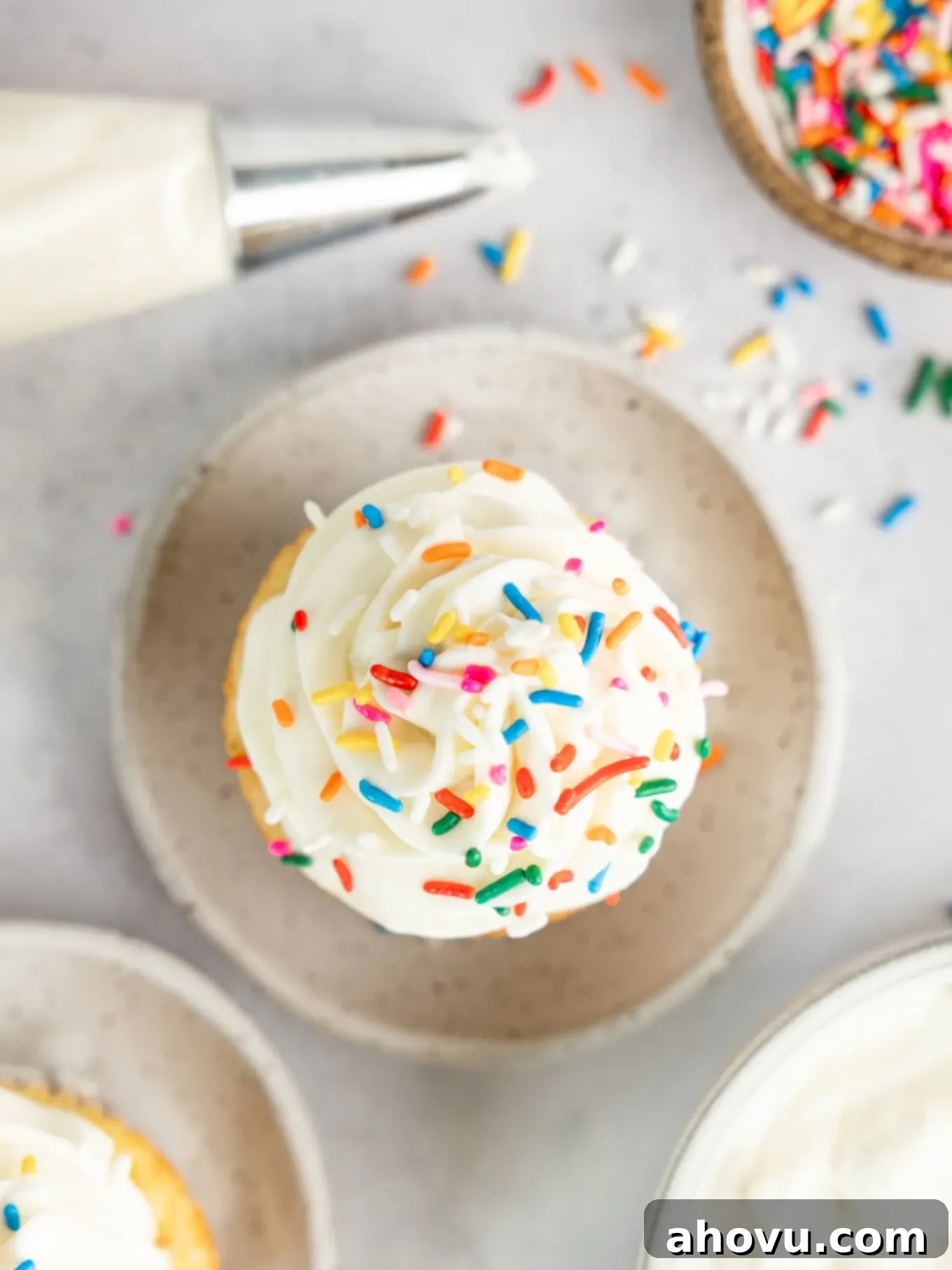 Overhead view of a perfectly frosted cupcake with whipped cream cheese frosting and colorful sprinkles, ready to be enjoyed.