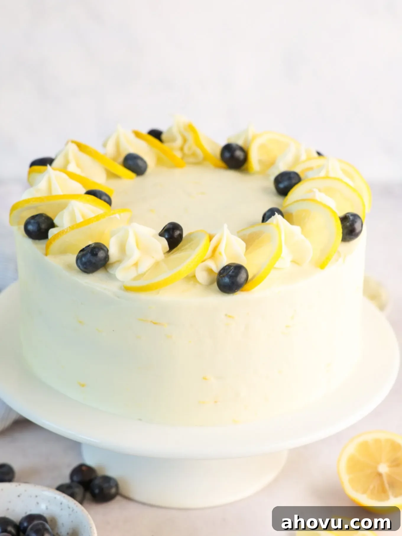 A stunning three-layer lemon blueberry cake, beautifully frosted and garnished with fresh blueberries and lemon slices, displayed on an elegant cake stand.